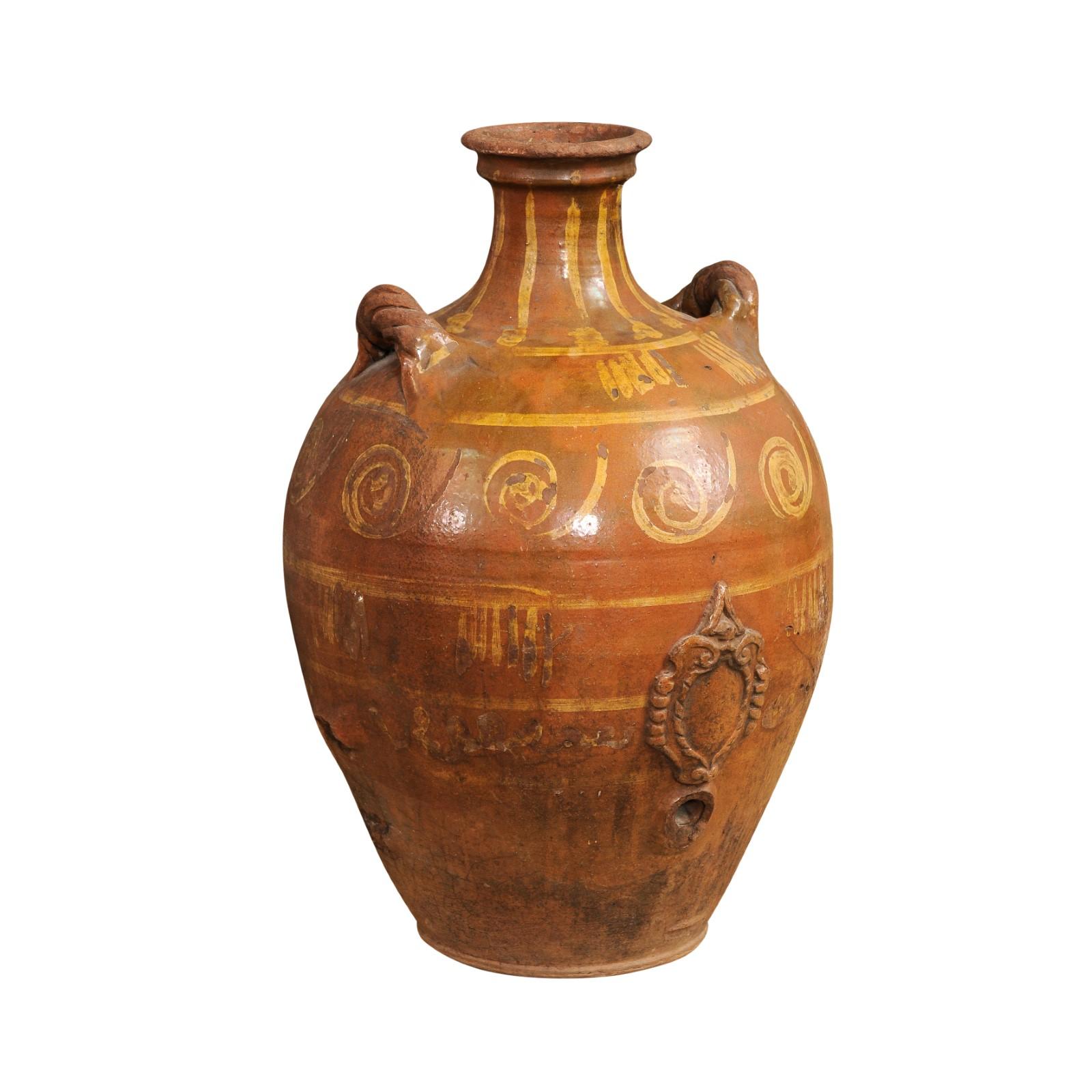 An Italian terracotta olive oil jar from the 17th century, with yellow glazed spiraling décor, raised motif and twisted lateral handles. Created in Italy during the 17th century, this terracotta olive jar features a brown ground highlighted by a