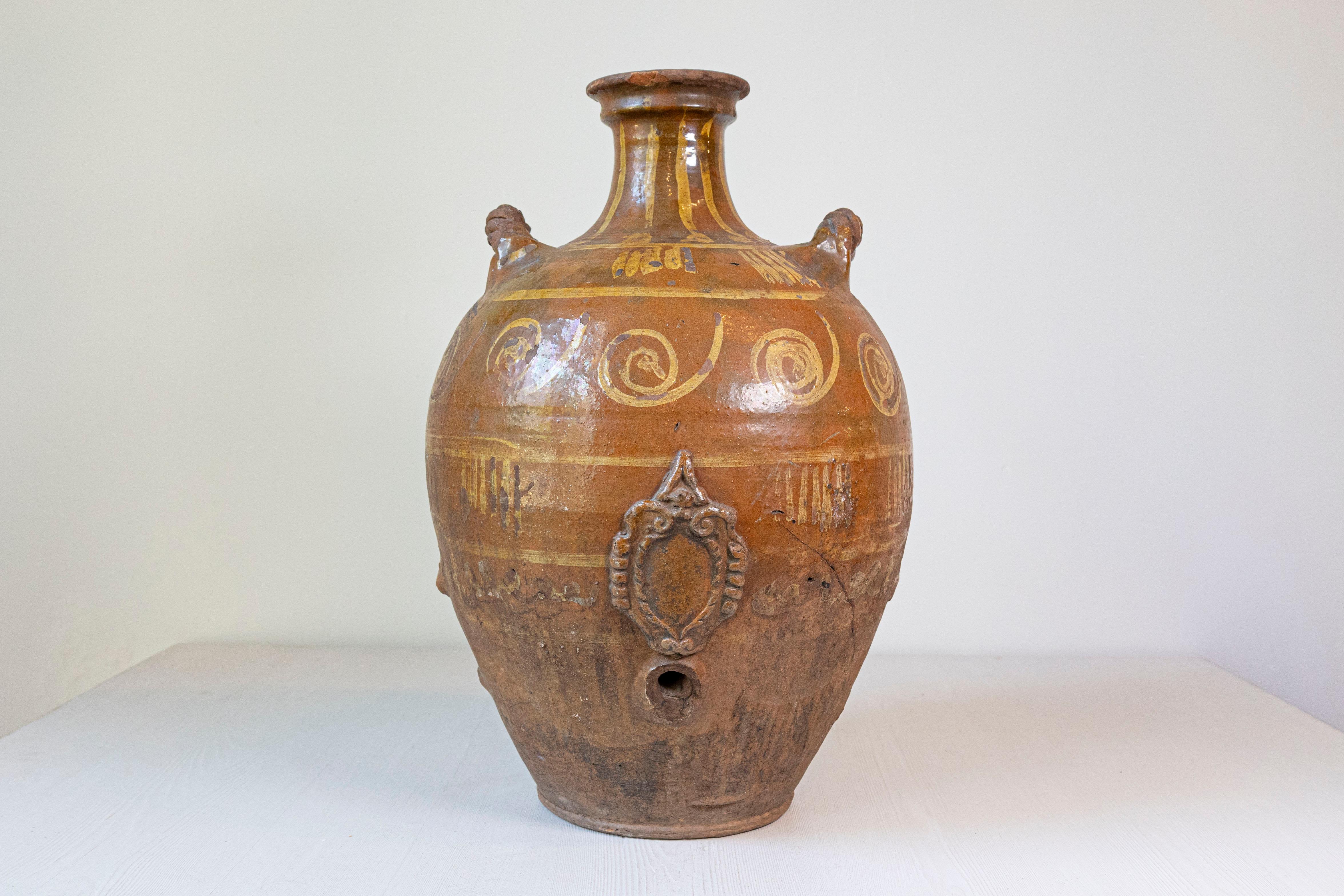An Italian terracotta olive oil jar from the 17th century, with yellow glazed spiraling décor, raised motif and twisted lateral handles. Created in Italy during the 17th century, this terracotta olive jar features a brown ground highlighted by a