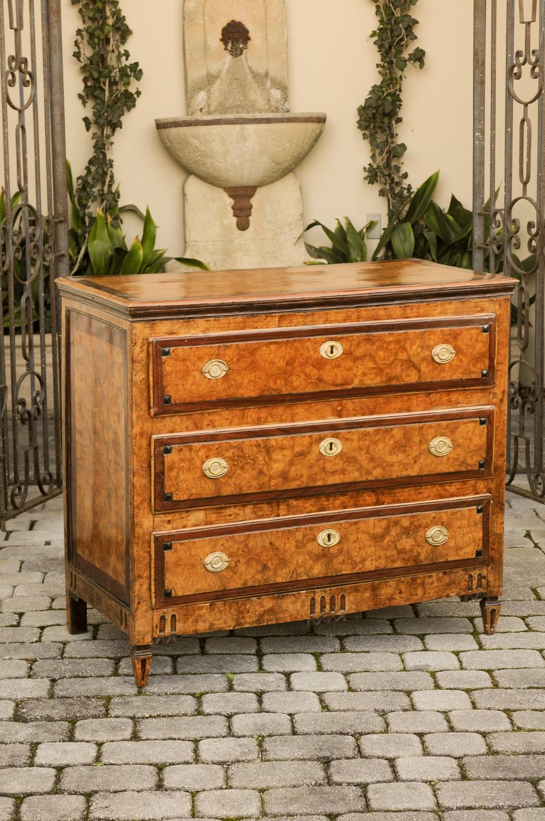 An Italian burl wood three-drawer commode from the early 19th century, with radiating veneer and fluted accents. Born in Italy during the early years of the 19th century, this elegant commode features an exquisite rectangular top, adorned with