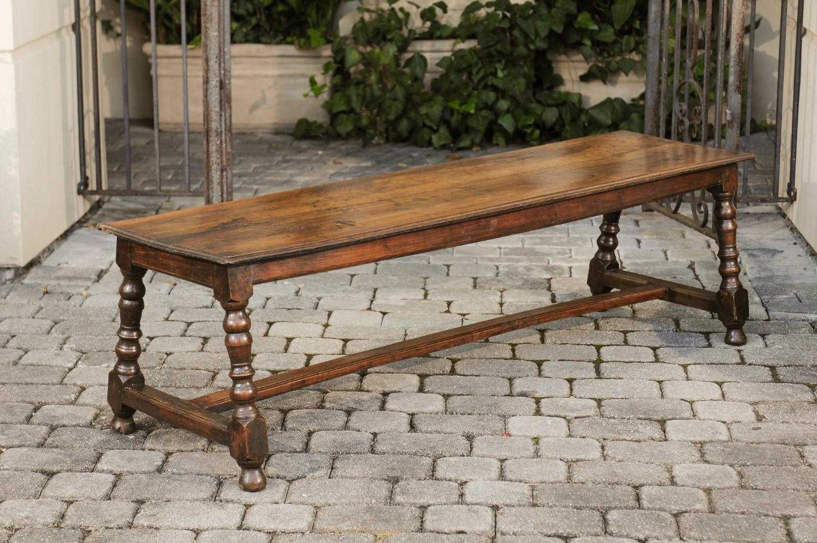 An Italian walnut bench from the early 19th century, with turned legs and cross stretcher. Born in Italy during the early years of the 19th century, this walnut bench features a rectangular top sitting above four splaying turned legs connected to