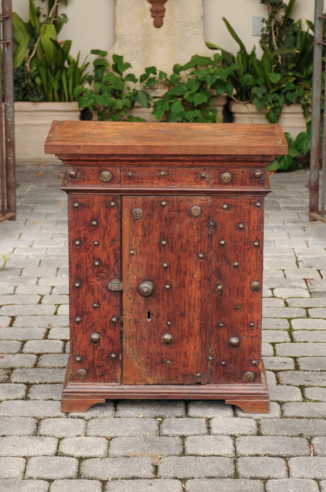 An Italian walnut cabinet from the early 19th century, with metal studs and single door. Born in Italy during the early years of the 19th century, this elegant small cabinet features a rectangular top sitting above a lovely apron with beveled