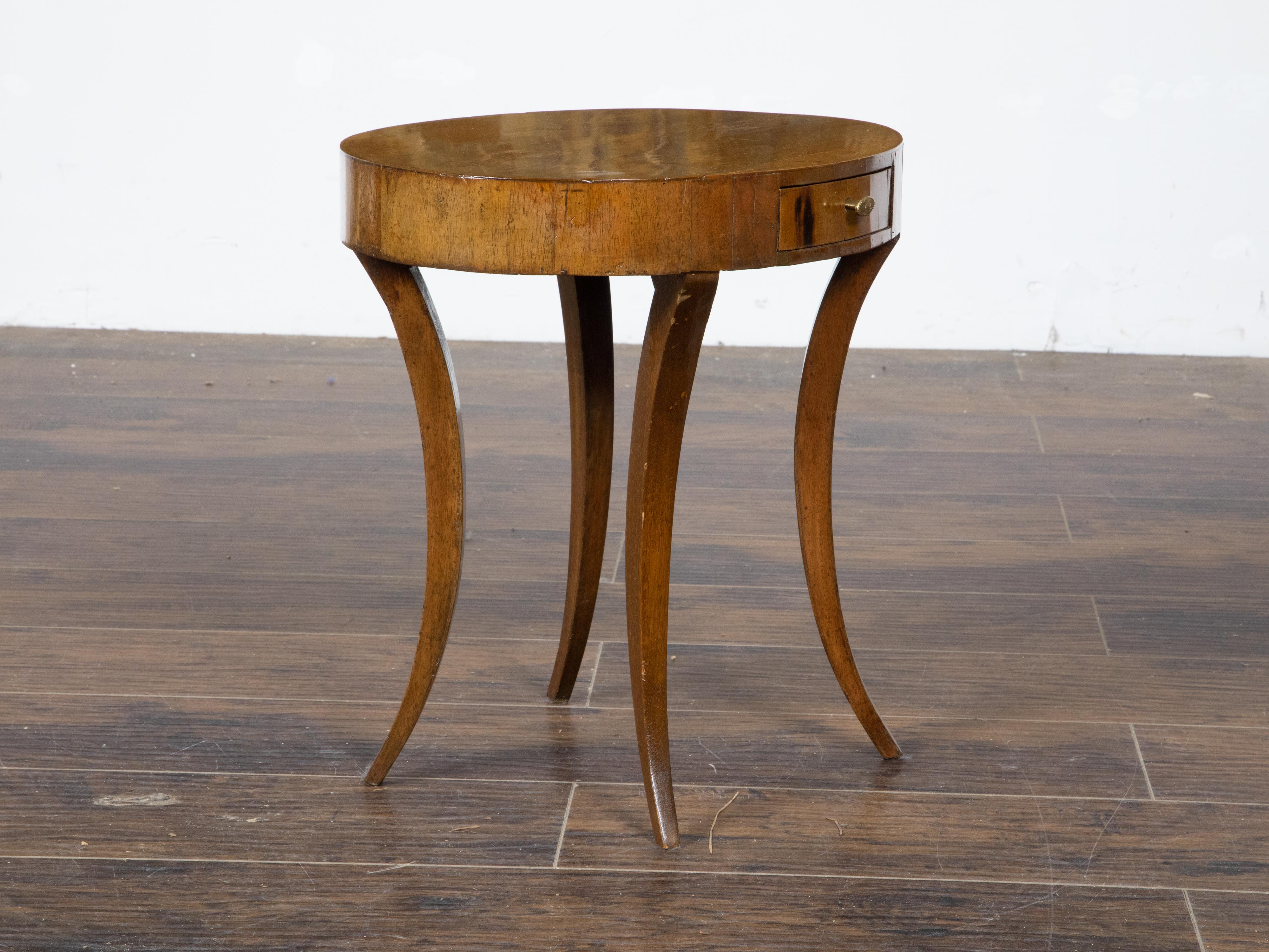 An Italian Neoclassical walnut veneered accent table from the early 19th century, with oval top, single drawer, brass hardware and saber legs. Created in Italy during the early years of the 19th century, this walnut accent table features an oval top