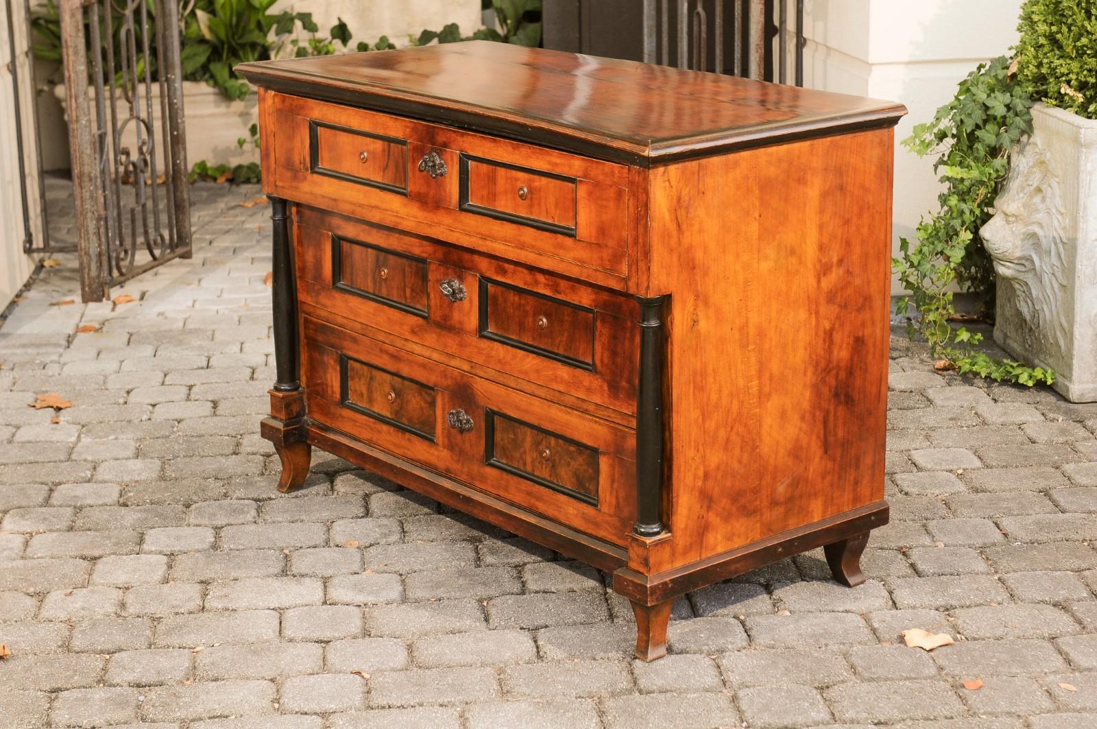 An Italian Empire walnut three-drawer commode from the early 19th century, with ebonized columns and saber feet. Born in Italy during the early years of the 19th century, this Italian Empire commode features a rectangular top with darker beveled