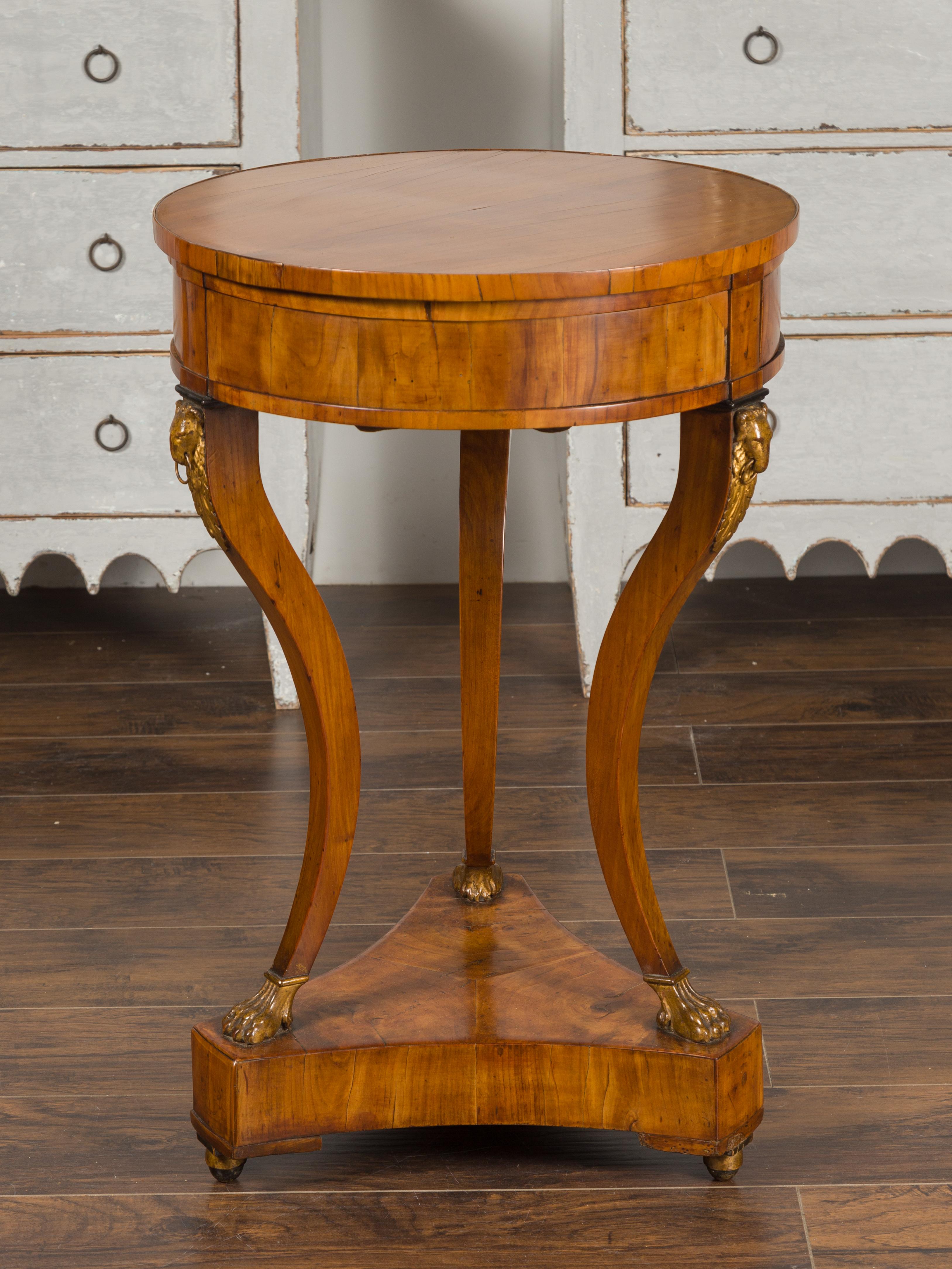 An Italian Empire walnut guéridon table from the early 19th century, with three pop-out drawers and gilt rams' heads. Born in Italy during the first quarter of the 19th century, this guéridon table features a circular top sitting above three pop-out