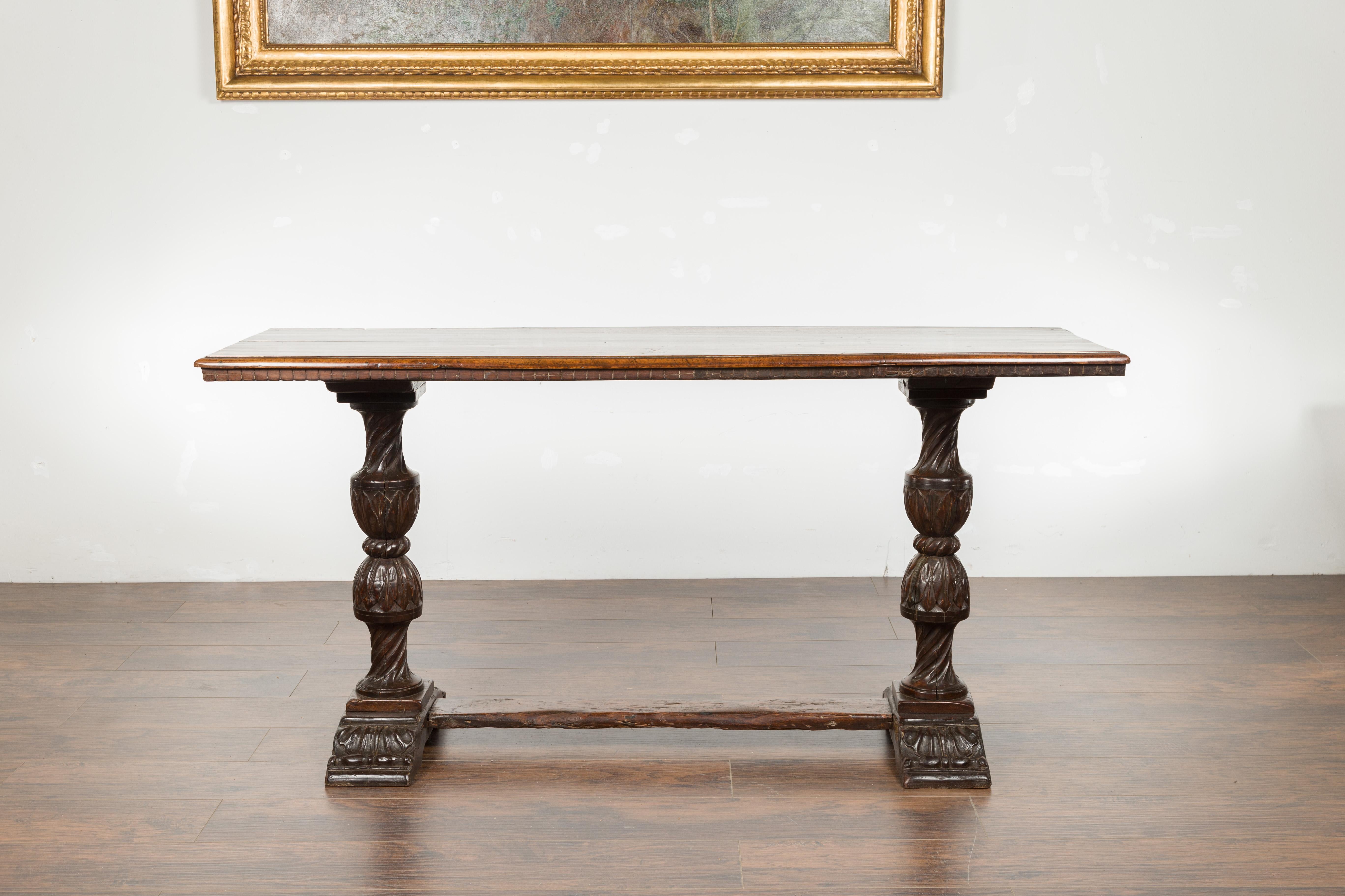 An Italian walnut console table from the early 19th century, with dentil molding, carved legs and cross stretcher. Created in Italy during the first quarter of the 19th century, this walnut table features a rectangular top with darker accent in the