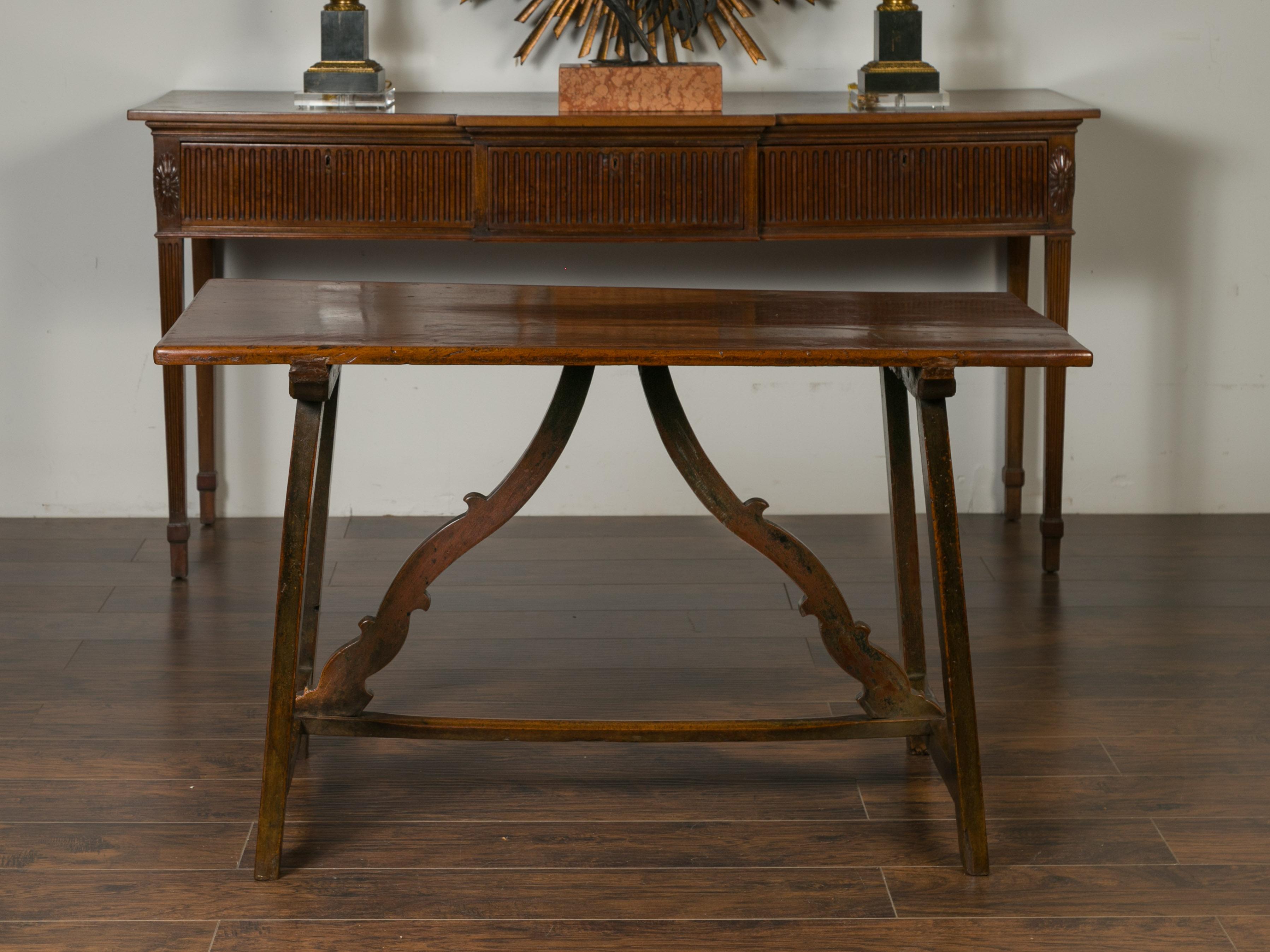 An Italian walnut console table from the early 19th century, with carved stretcher. Born in Italy during the first quarter of the 19th century, this walnut console table feature a rectangular top sitting above a trestle base. The simple splaying