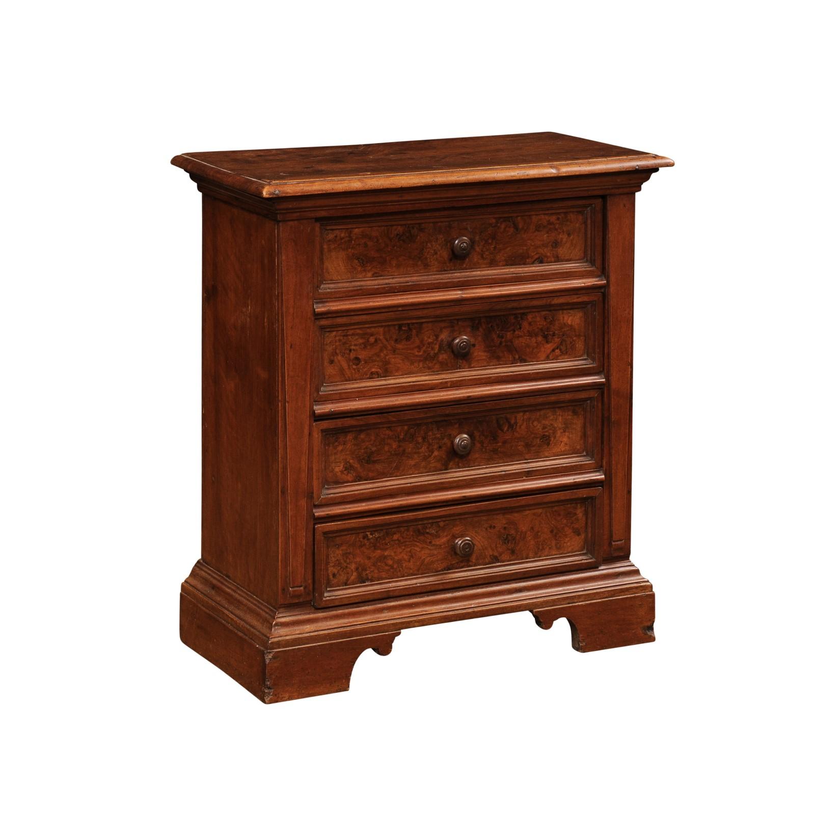 An Italian walnut bedside chest from circa 1840 with burl wood panels, four drawers and carved bracket feet. Immerse yourself in the grandeur of 19th-century Italian craftsmanship with this captivating walnut bedside chest from circa 1840. This