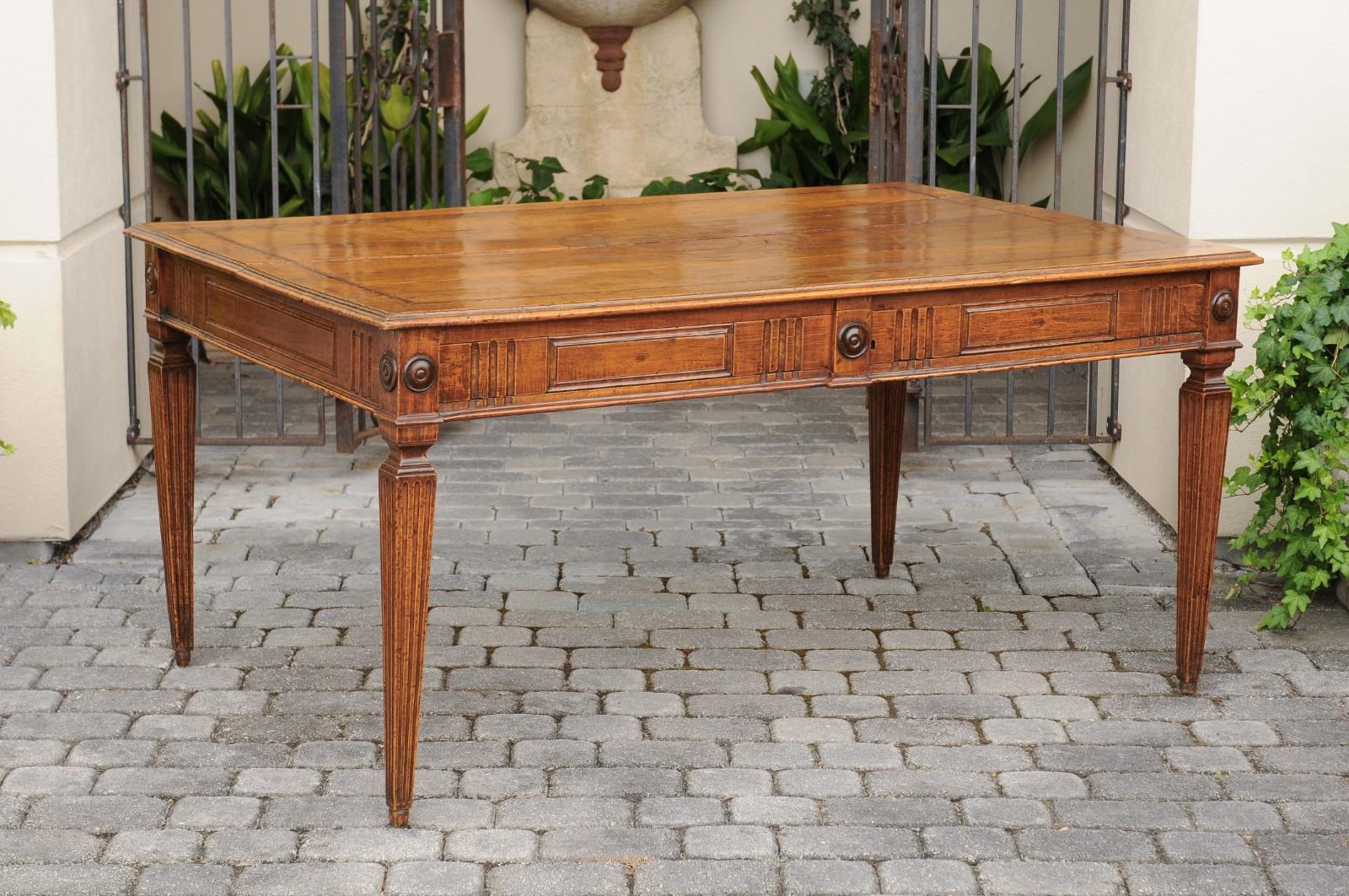 An Italian walnut desk from the mid-19th century with inlaid top, fluted accents and tapered legs. Born in Italy during the 1850s, this walnut writing table features a rectangular top with floral inlay, sitting above an exquisite apron adorned with