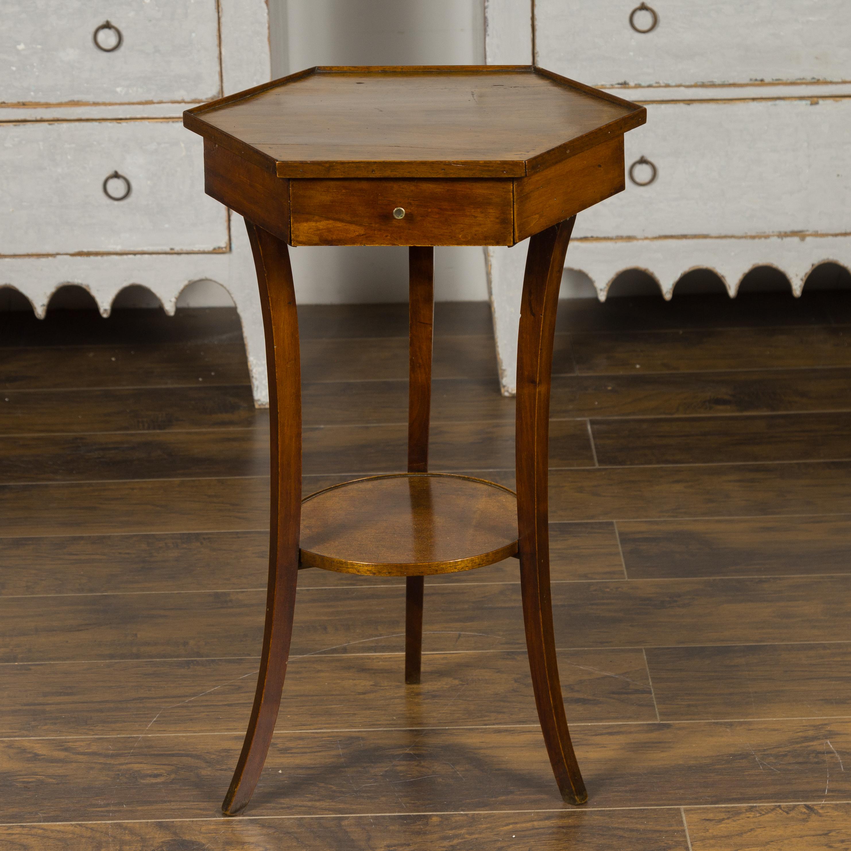 An Italian walnut hexagonal table from the mid 19th century, with single drawer and lower shelf. Born in Italy during the 1850s, this walnut side table features an hexagonal top sitting above a single drawer fitted with a petite brass pull. The