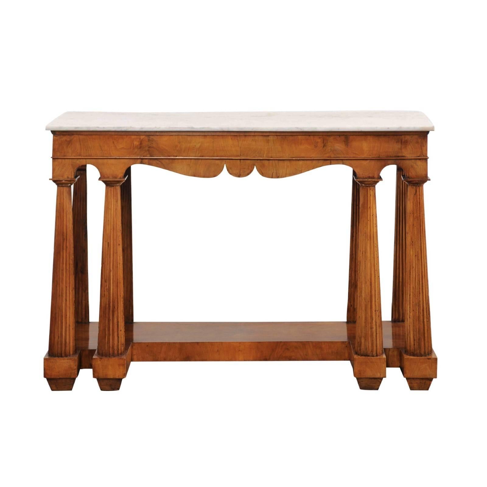 An Italian walnut veneered console table with white marble top, scalloped apron and fluted legs from the mid-19th century. This Italian console table features a rectangular white marble top, surmounting an exquisite bookmark-veneered apron with