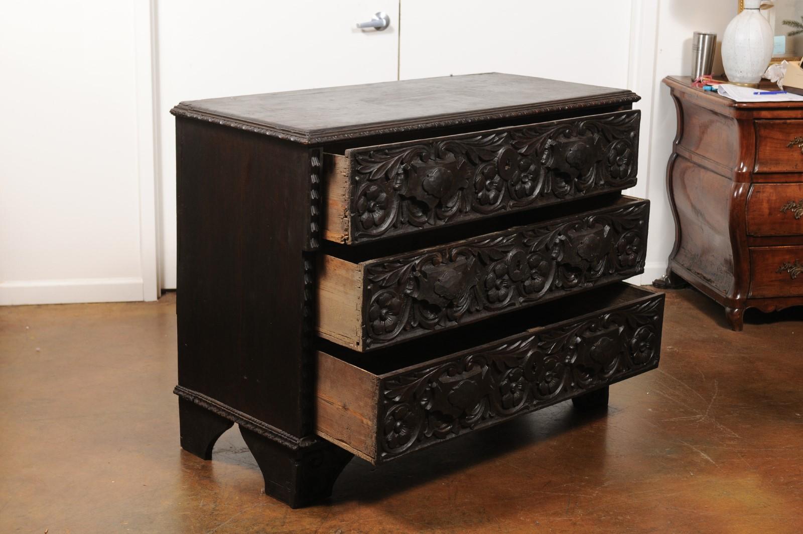 An Italian wooden three-drawer chest from the mid 19th century, with hand-carved scrollwork décor and dark patina. Born in Italy during the third quarter of the 19th century, this commode will charm you with its exquisite hand-carved décor of