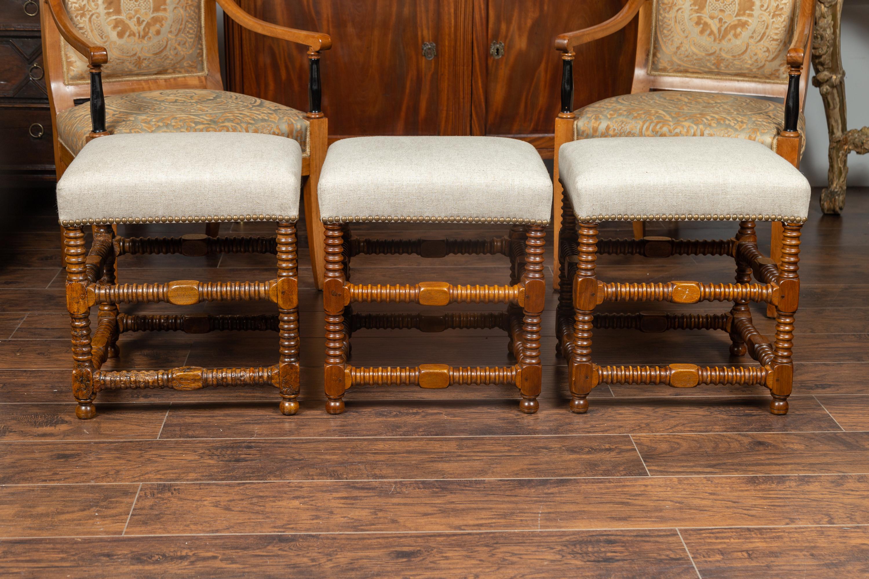 One Italian spool legs walnut stool is available. Born in Italy during the third quarter of the 19th century, it features a rectangular seat newly recovered with new linen upholstery accented with brass nailhead trim. Raised on four spool legs with