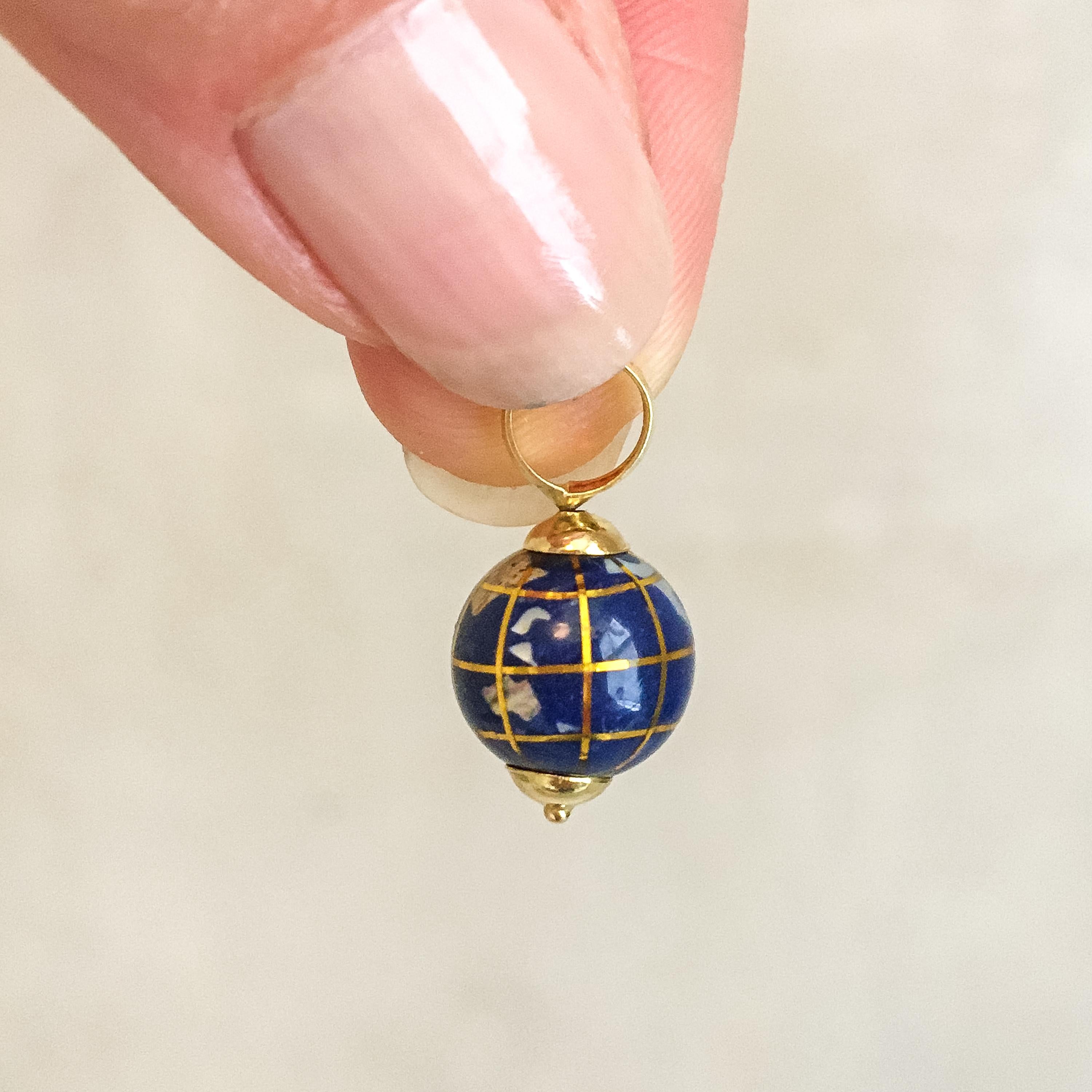 An 18 karat yellow gold pendant in the shape of a globe, made of porcelain containing several continents and islands. These are inlaid with mother-of-pearl and semi-precious stones, including Aventurine, Jasper and Peridot. The porcelain is finished