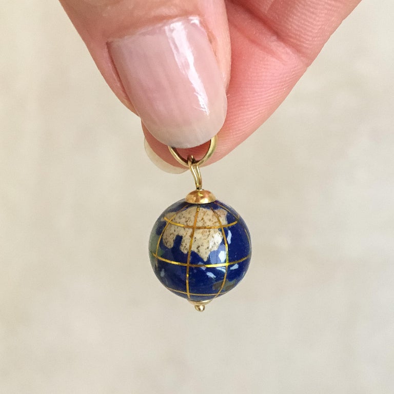 A beautiful 18 karat gold pendant in the shape of a globe, made of porcelain containing several continents and islands. These are inlaid with mother-of-pearl and semi-precious stones, including Peridot, Aventurine and Jasper. The porcelain is