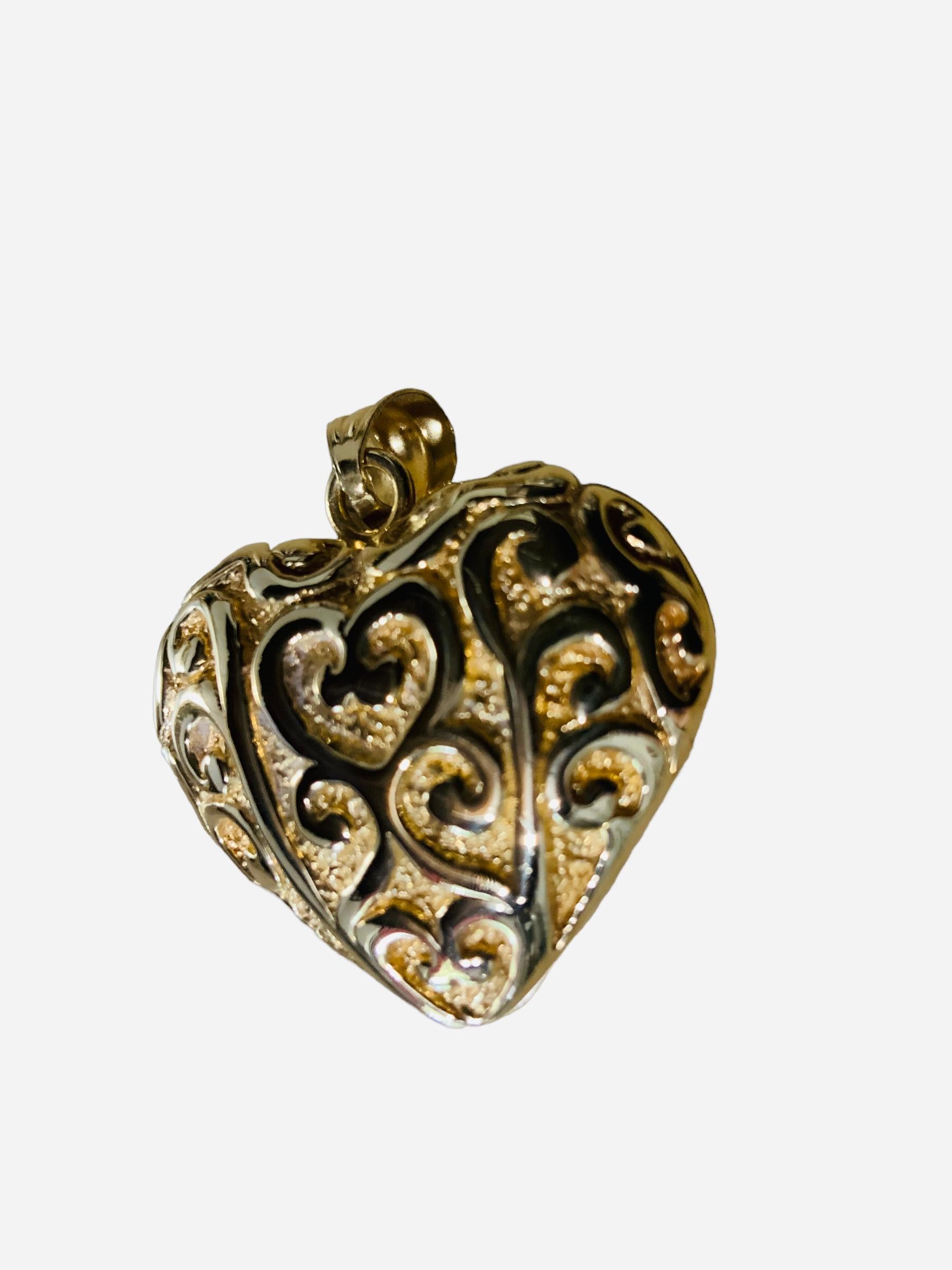 Questo è un ciondolo a forma di cuore in oro giallo 18 carati. Ha il marchio 750 nell'ansa e 18 carati, Italia e ZRW nella punta del cuore. Il ciondolo a forma di cuore è ornato da un disegno in rilievo di cuori al centro e da diverse volute che li