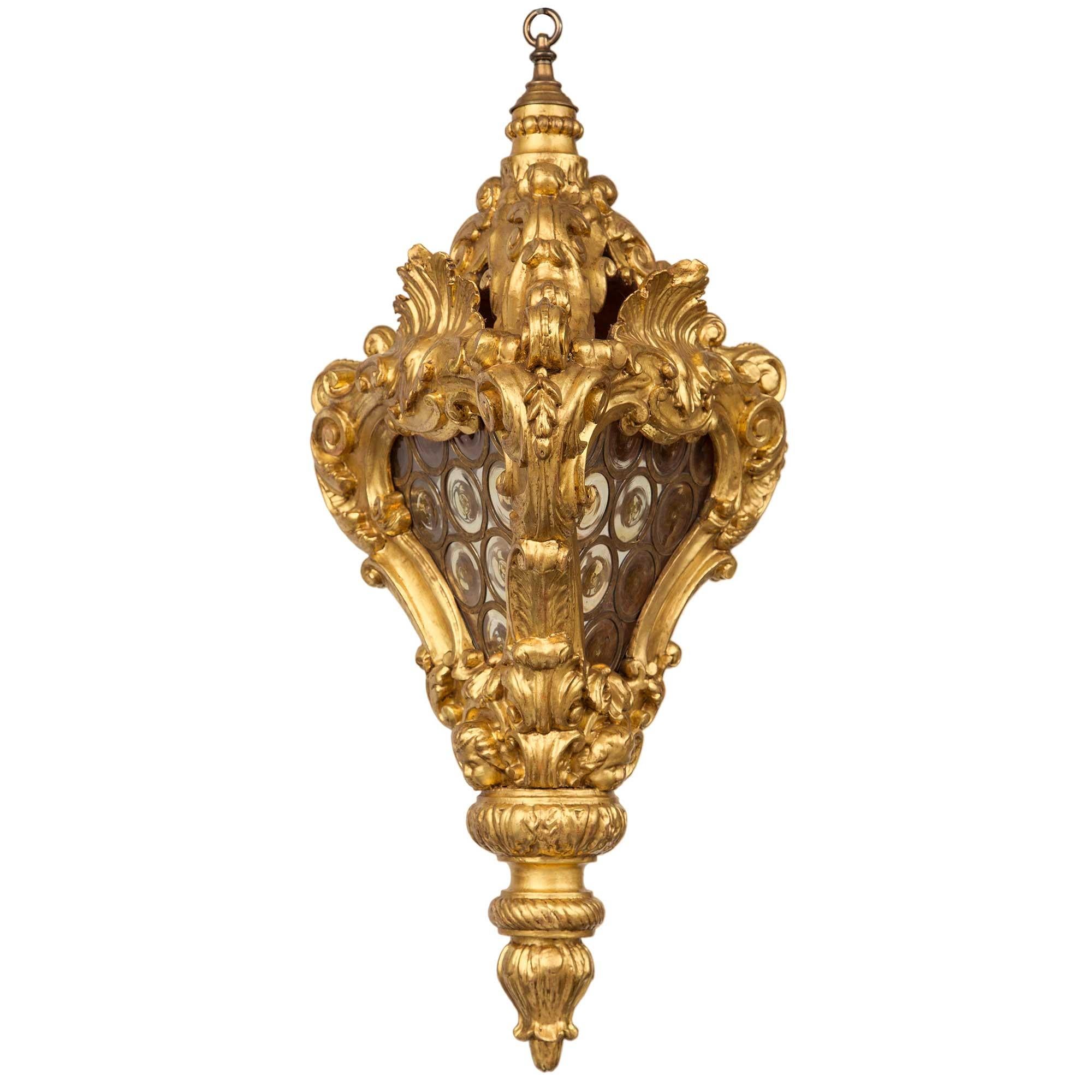 A striking and most unique Italian 18th century Baroque period giltwood and glass lantern. The lantern is centered by a bottom foliate finial with a wrap around twisted design. Above an acanthus leaf border is a charming cherub's head amidst rich