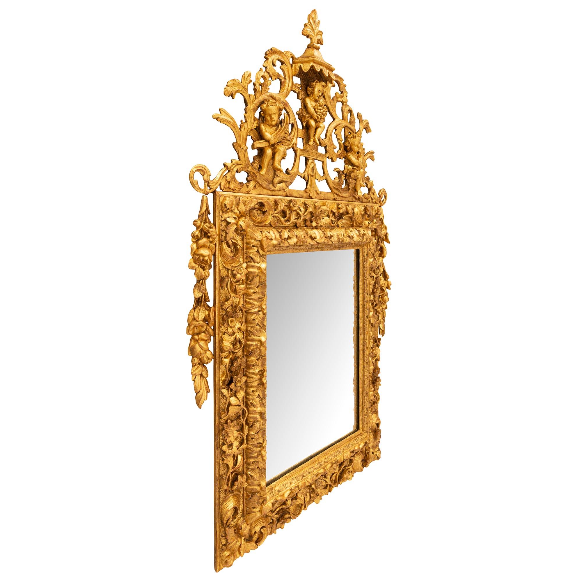 Remarquable miroir en bois doré d'époque baroque italienne du XVIIIe siècle. La plaque de miroir au centre est encadrée d'une très élégante bordure mouchetée avec de beaux motifs feuillagés richement ciselés et de jolies fleurs épanouies aux détails