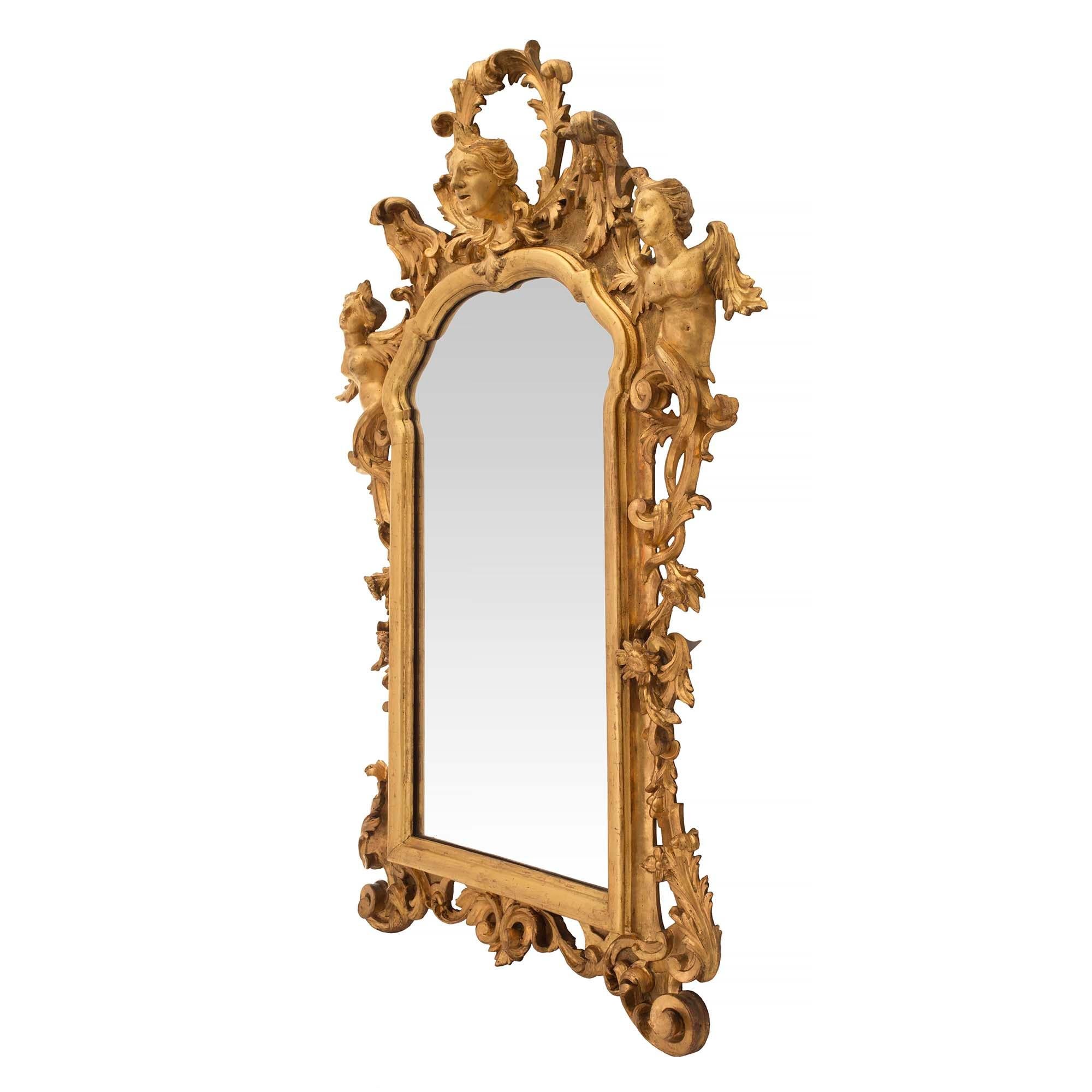An outstanding Italian 18th century Baroque style giltwood mirror. The mirror is raised by scrolled feet with large acanthus leaves and floral carvings centering the scrolled bottom reserve. Leading up each side are rich carvings of flowers and