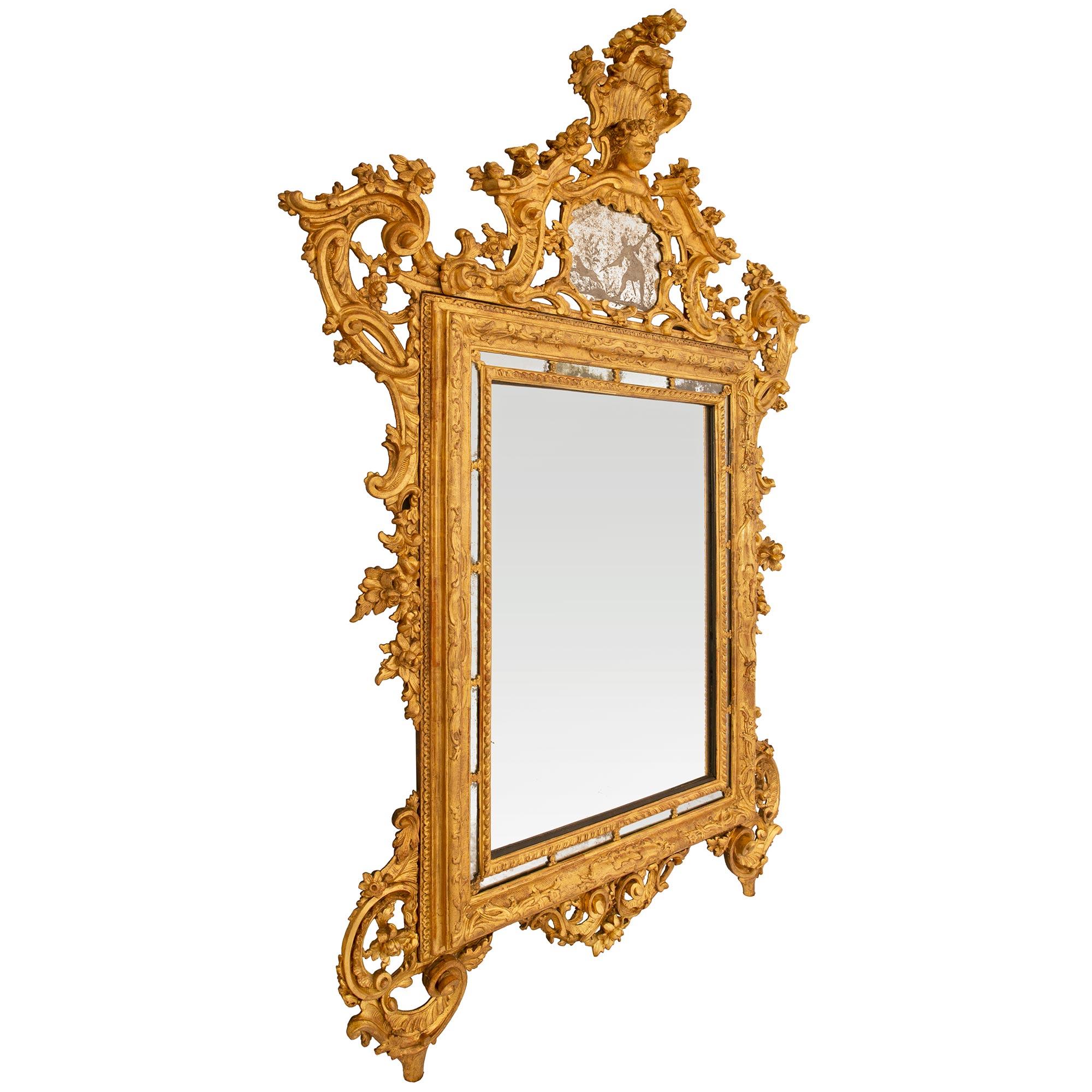 Miroir baroque italien du XVIIIe siècle en bois doré, de grande taille et de grande qualité, provenant de la collection de Hughes. Cet exquis miroir de sol repose sur deux pieds joliment enroulés, attachés à des décorations percées très finement