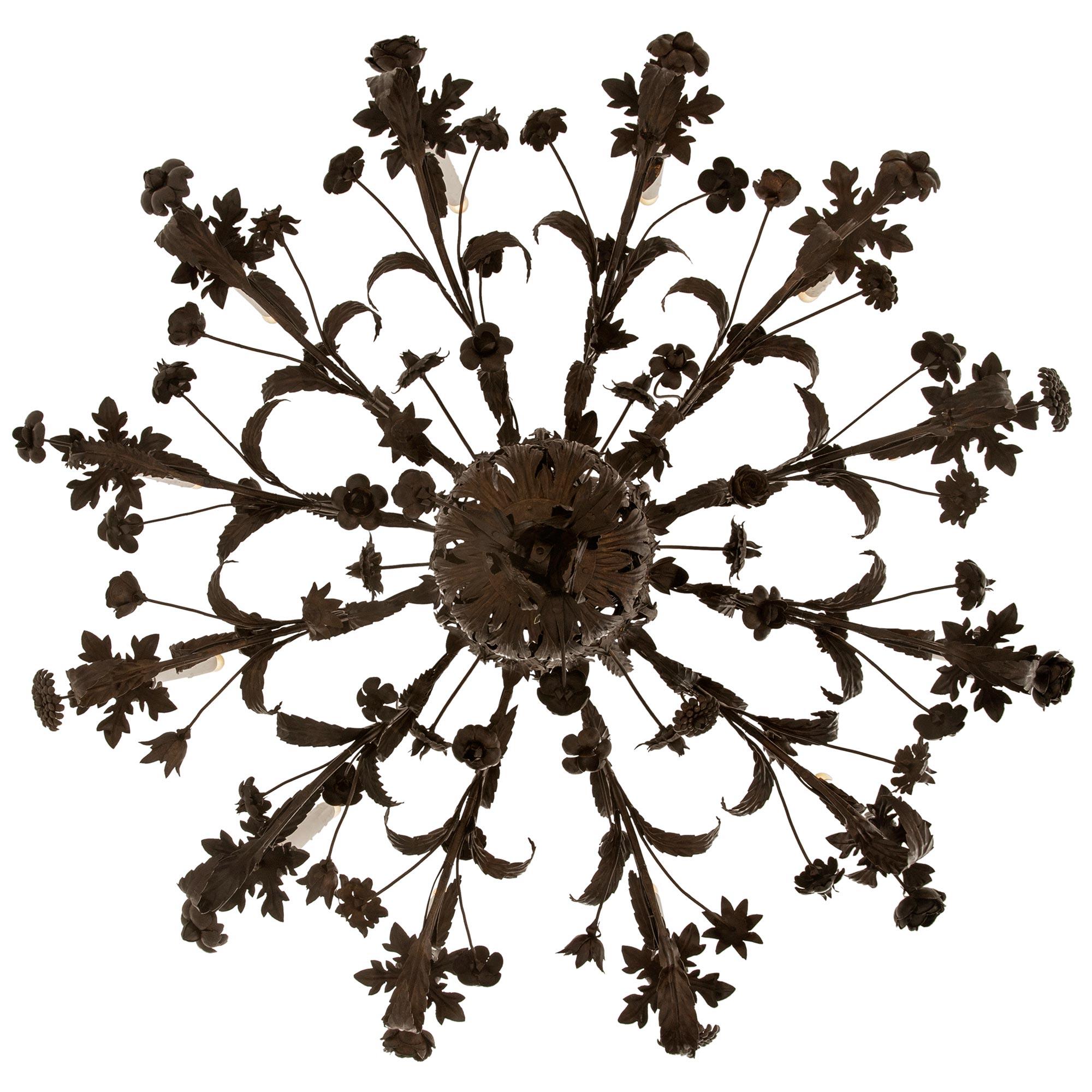 An extremely decorative and large scaled Italian 18th century Baroque st. patinated Bronze and Tole chandelier. The twelve arm chandelier is centered by a beautiful rounded array of acanthus leaves that surround the Bronze frame holding all of the