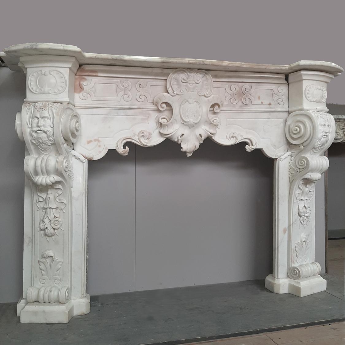 18th century Italian Carrara marble fireplace, richly decorated in the Baroque style. On the central cartouche of the mantlepiece a coat of arms. The legs decorated with scrolls, masks of fauns above festoons of flowers and acanthus leafs.