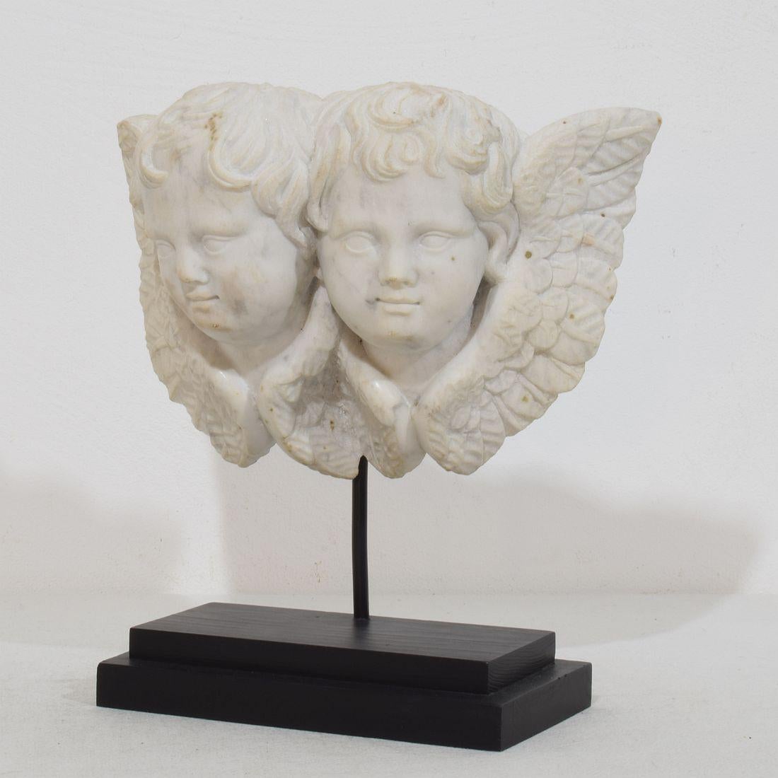 Beautiful and unique handcarved white marble winged  double angel head ornament.
Italy, circa 1750.
Weathered .
Measurement includes the wooden base.
H:24cm  W:23cm D:10cm 