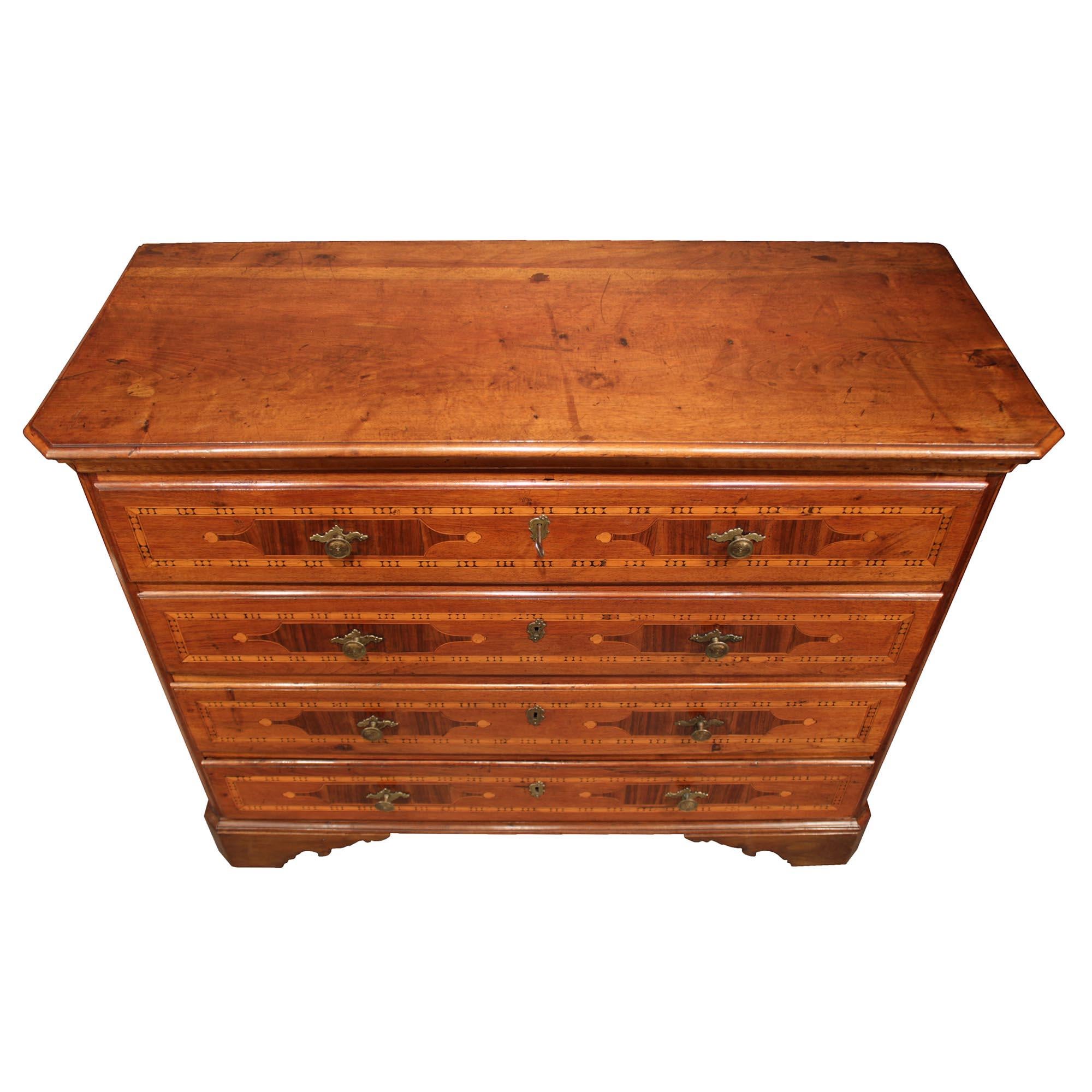 A handsome Italian 18th-century country four-drawer pine and walnut chest. The chest is raised on scalloped supports below a mottled straight frieze. Each of the four drawers retains their original brass keyhole escutcheons and pulls and are