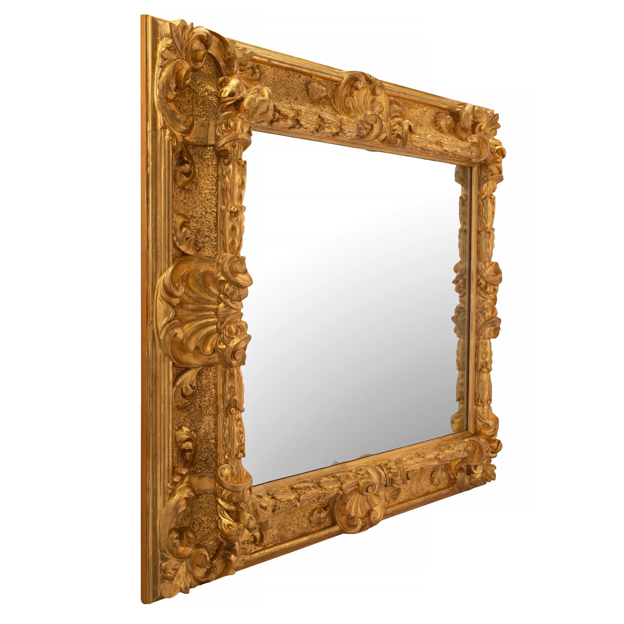 Superbe miroir italien en bois doré florentin du XVIIIe siècle. La plaque de miroir est encadrée d'une belle bordure en bois doré avec une fine bande de lauriers et un motif moucheté. À chaque angle, de fins mouvements feuillagés en volutes centrent