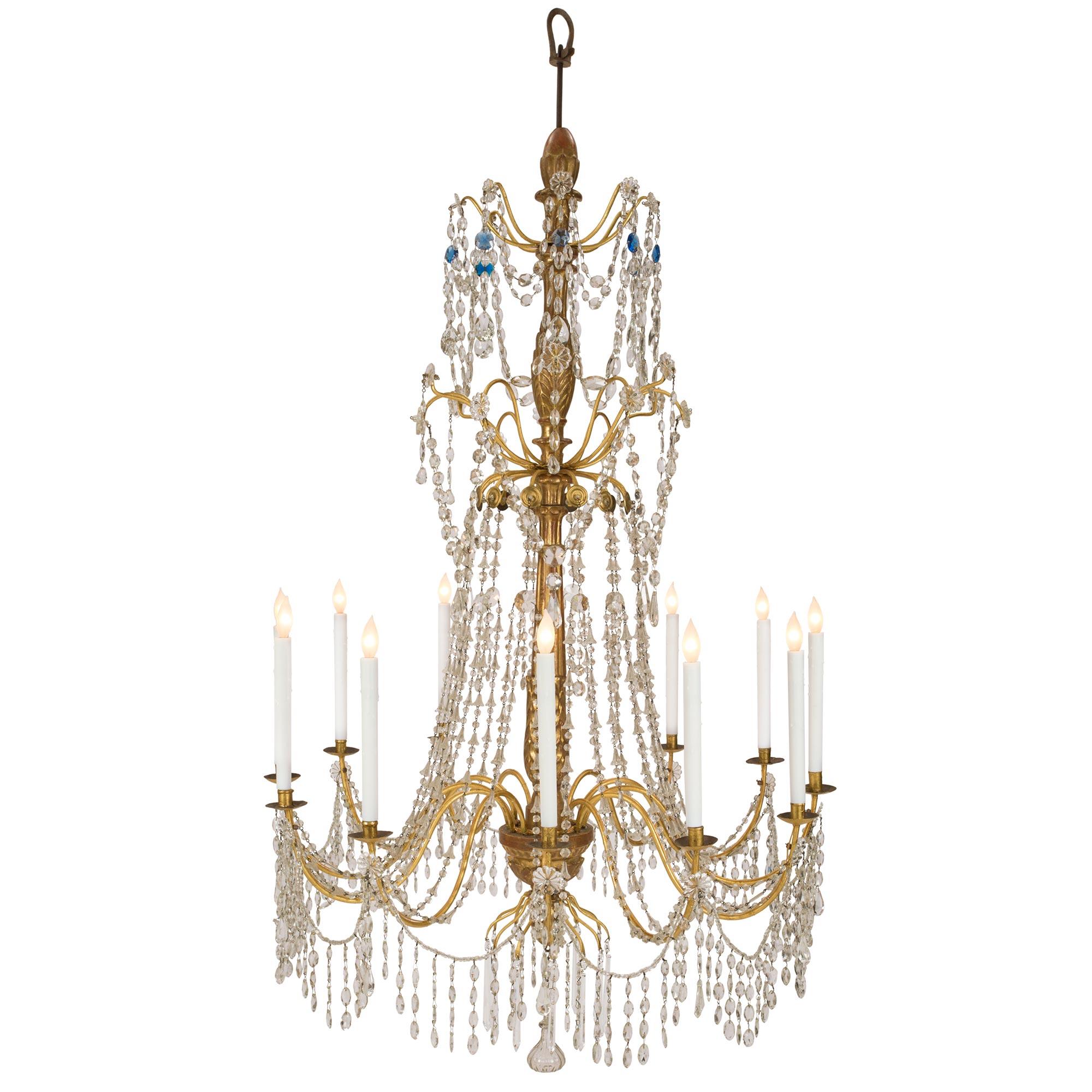 An impressive and large scale Italian 18th century giltwood and gilt iron chandelier with clear and blue colored crystals and glass garlands. The twelve scrolled gilt metal arms are decorated by crystal drops topped by rosettes and are joined by