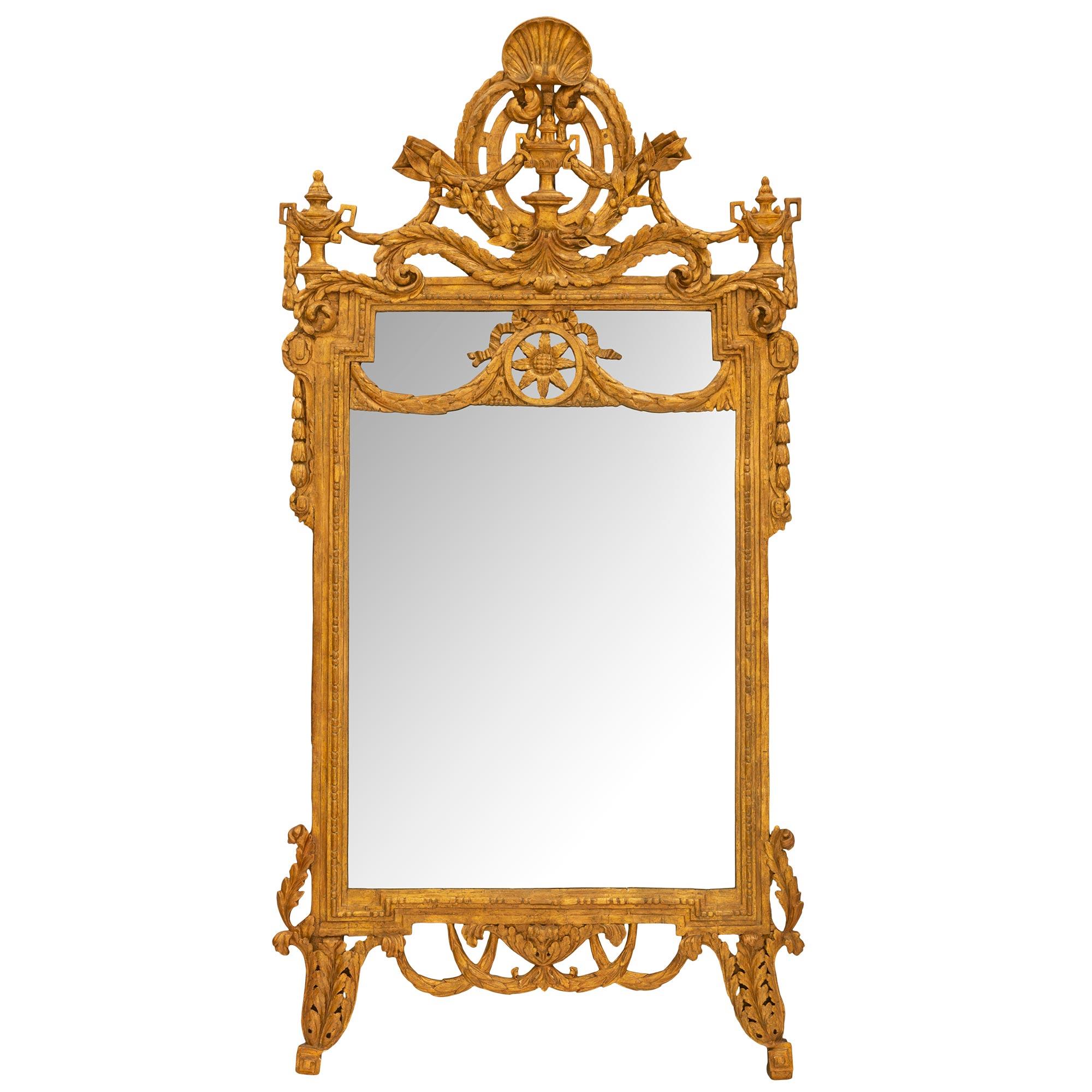 A spectacular early 18th century Italian giltwood mirror, circa 1730. The mirror is raised on richly carved acanthus leaf supports. The egg and dart border is joined at the top with a pierced central rosette medallion draping laurel garland topped