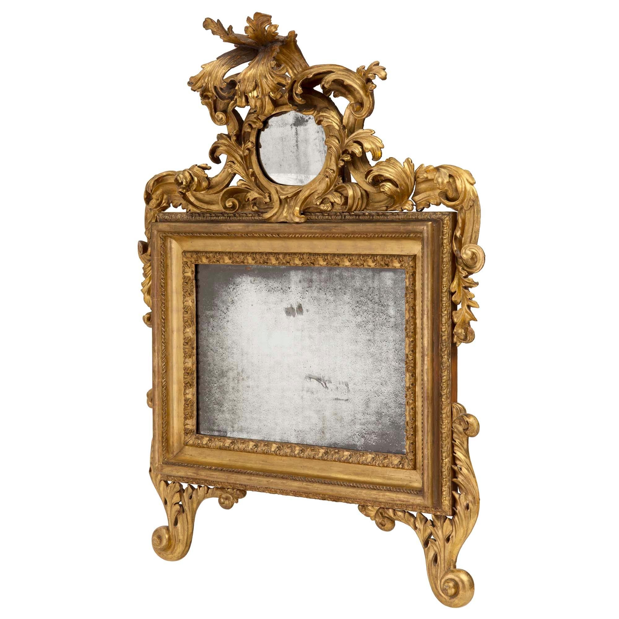 Un impressionnant miroir romain en bois doré italien du XVIIIe siècle. Le miroir est surélevé par de magnifiques pieds à volutes et à motifs de feuillages. Le miroir central d'origine est encadré d'une bordure richement sculptée de feuillages