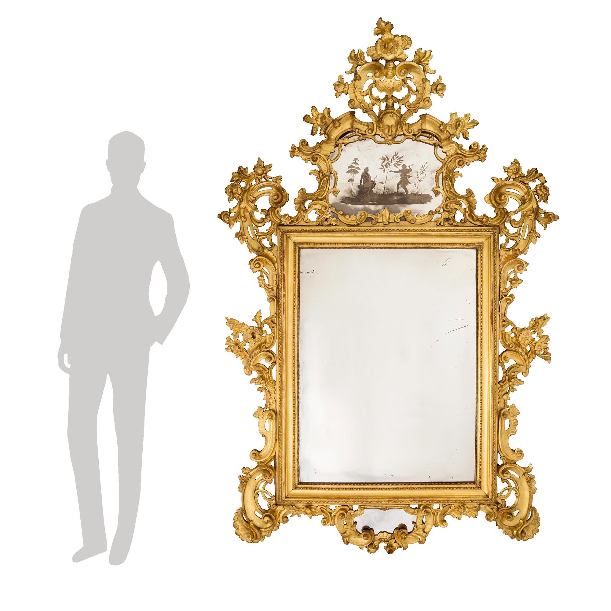 A magnificent Italian 18th century giltwood Venetian mirror. This finely carved mirror has original mirror plates and is sumptuously adorned with scrolled foliate and garlands. At the bottom is a mirror amidst scrolled giltwood. Continuing up each