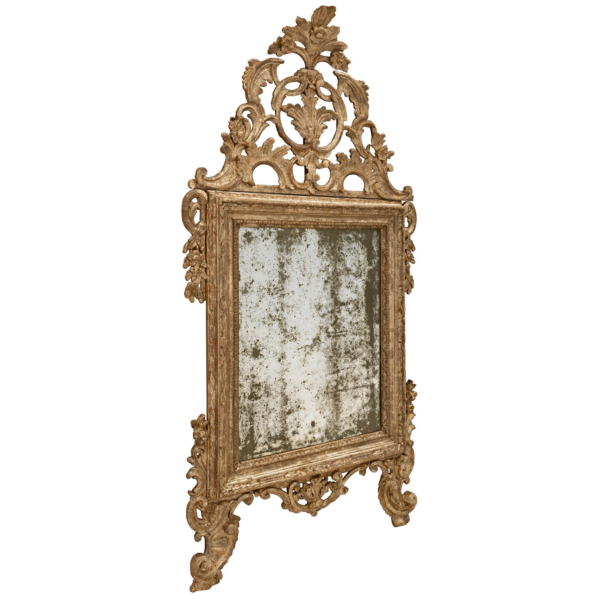 A very unique Italian 18th century Louis XIV period white gold mecca mirror. The two scrolled feet are joined by a pieced acanthus leaf garland. The original mirror plate is framed within the mottled border with rich foliate carvings at each corner.