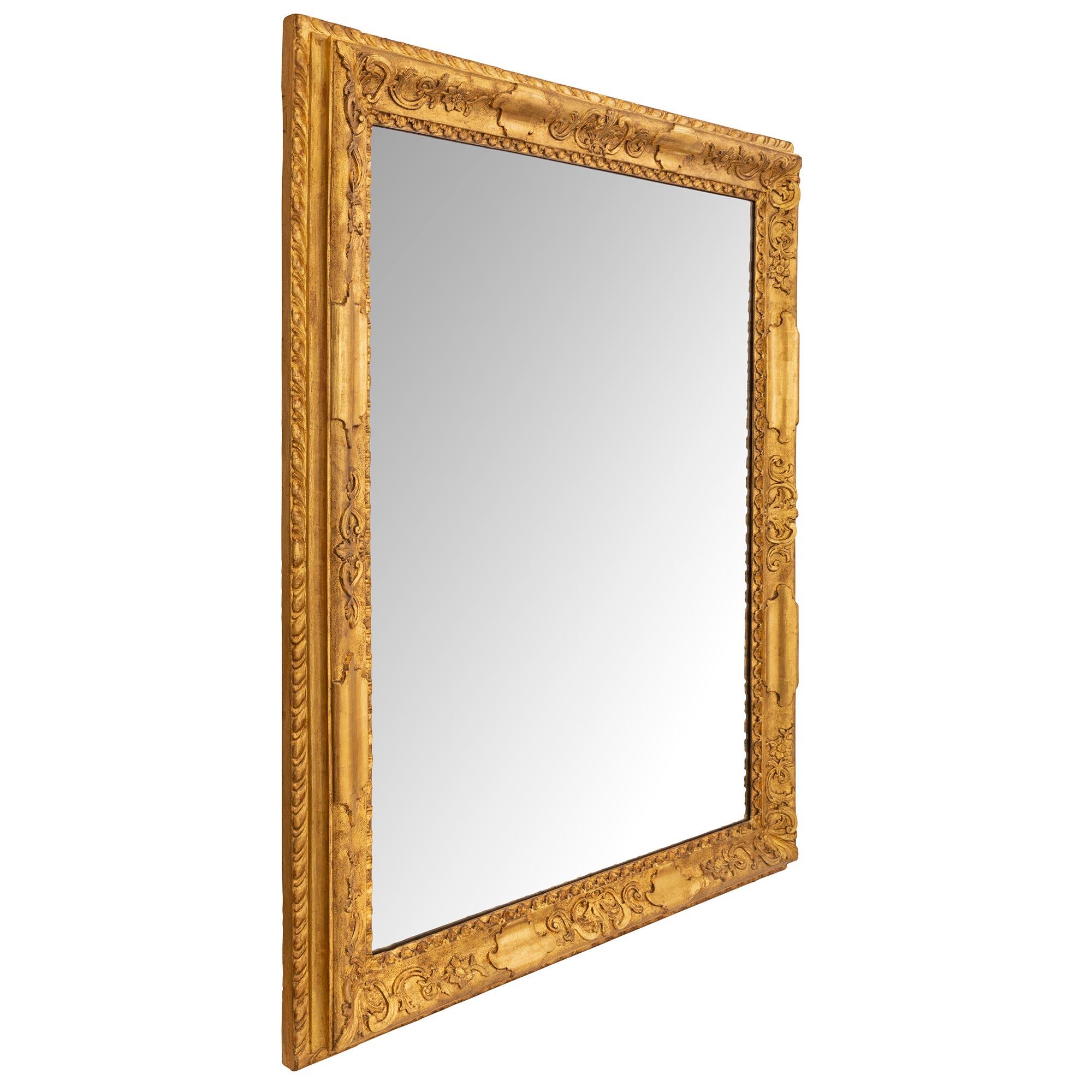 Un élégant miroir italien du 18ème siècle en bois doré de style Louis XIV. La plaque centrale du miroir est placée dans un magnifique cadre en bois doré moucheté avec des motifs feuillus finement détaillés et une bande enveloppante à godrons sur la