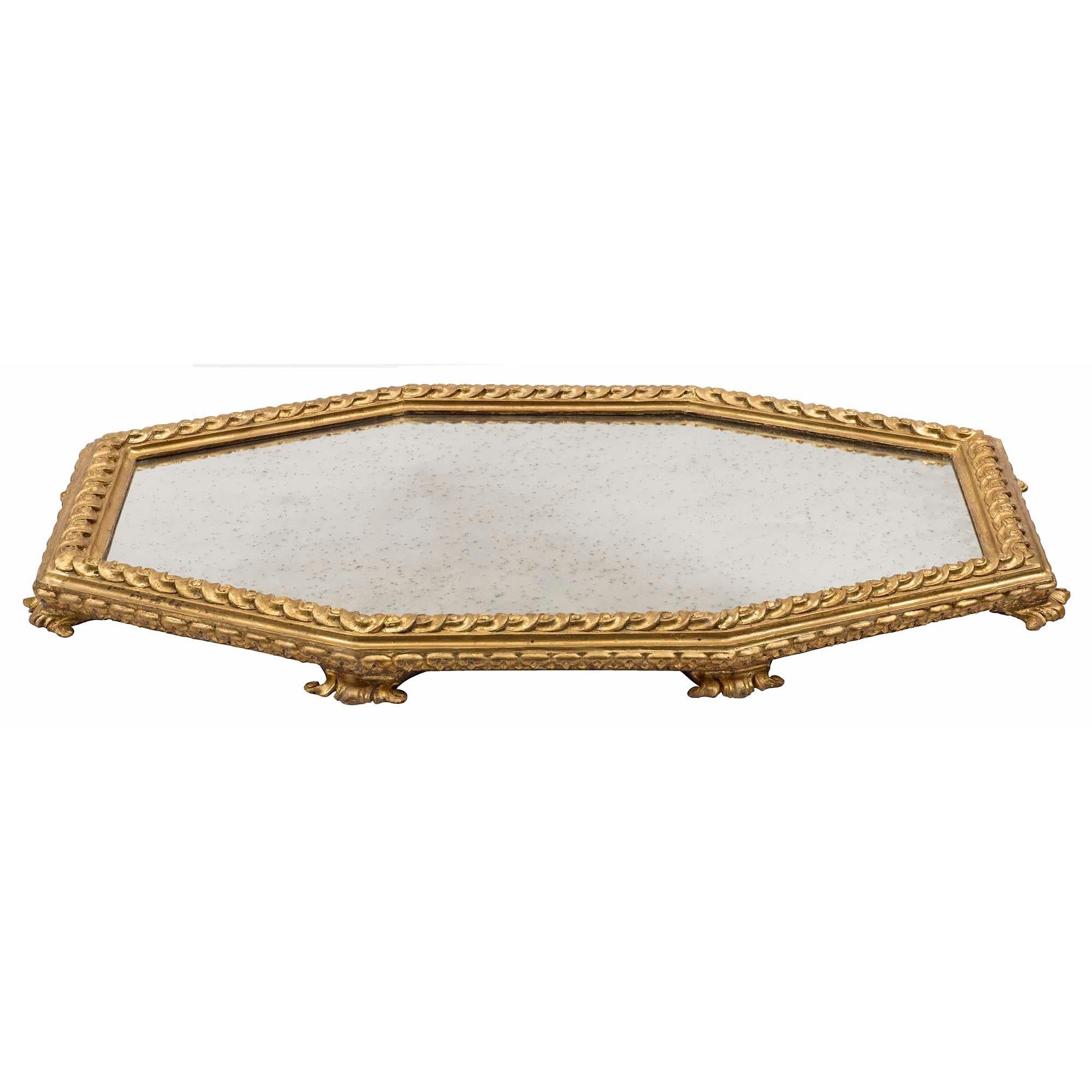 A very handsome Italian 18th century Louis XVI period giltwood centerpiece. The elongated octagonal shaped surtout de table is raised by eight most decorative foliate feet below a foliate beaded band. Centering the original mirror plate is a richly