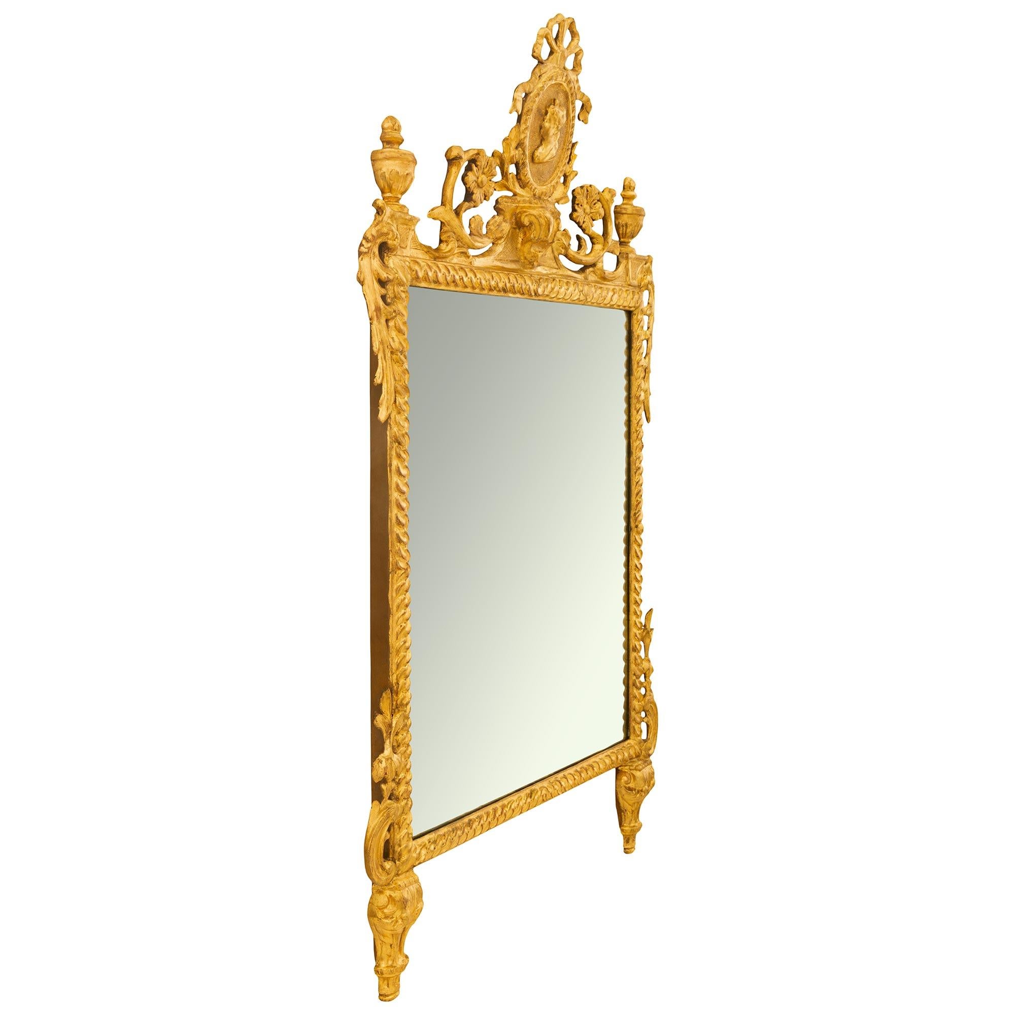 An elegant Italian 18th century Louis XVI period Giltwood mirror. The mirror with all of its original mirror plate and gilding is raised by two supports with acanthus leaves. The rectangular frame with a wavelike design has an ’S’ scrolled acanthus