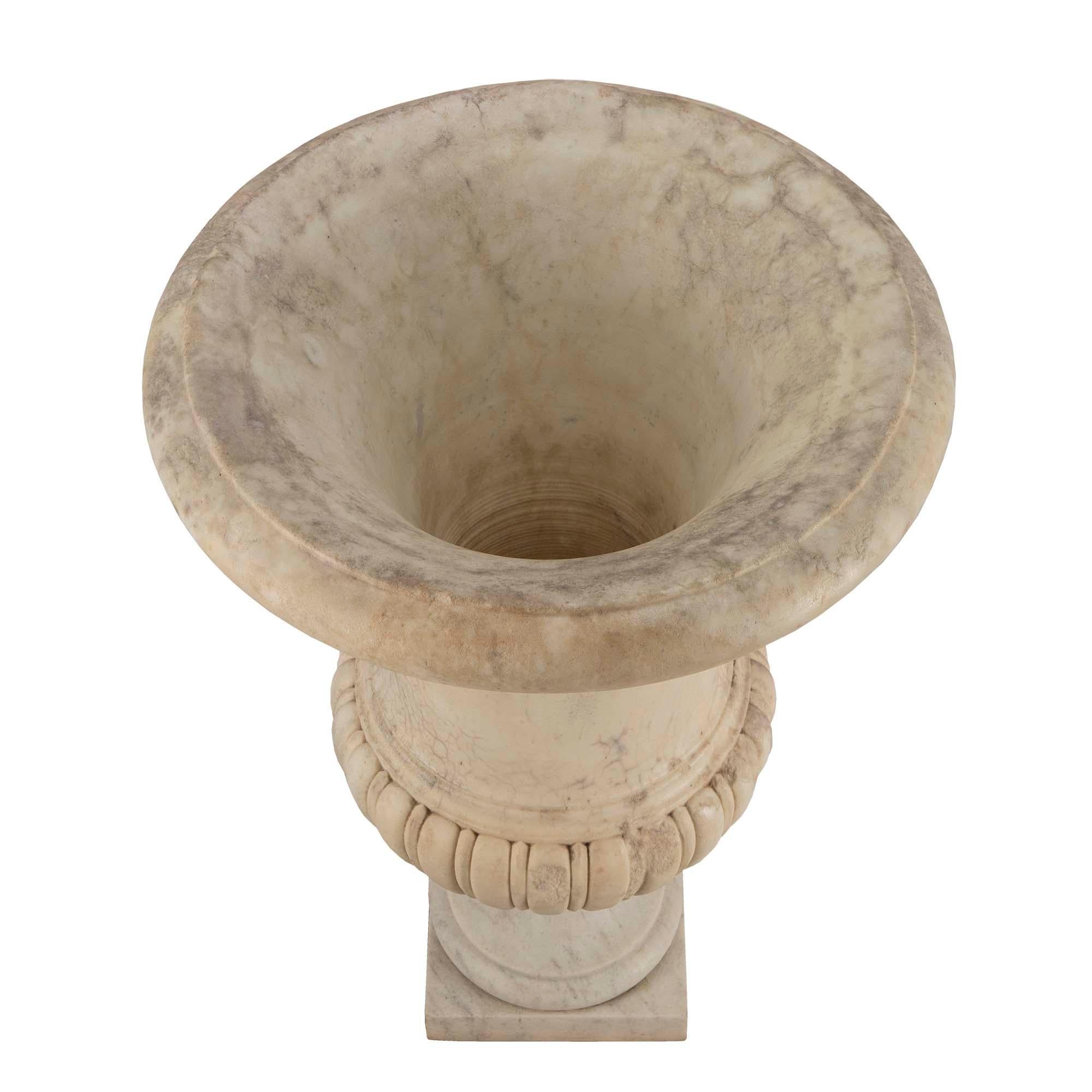 Una urna de mármol blanco de Carrara muy decorativa, italiana, del siglo XVIII, época de Luis XVI. La preciosa urna se eleva sobre una base cuadrada bajo el pedestal de zócalo moldeado. El cuerpo presenta un diseño de láminas finamente esculpido que