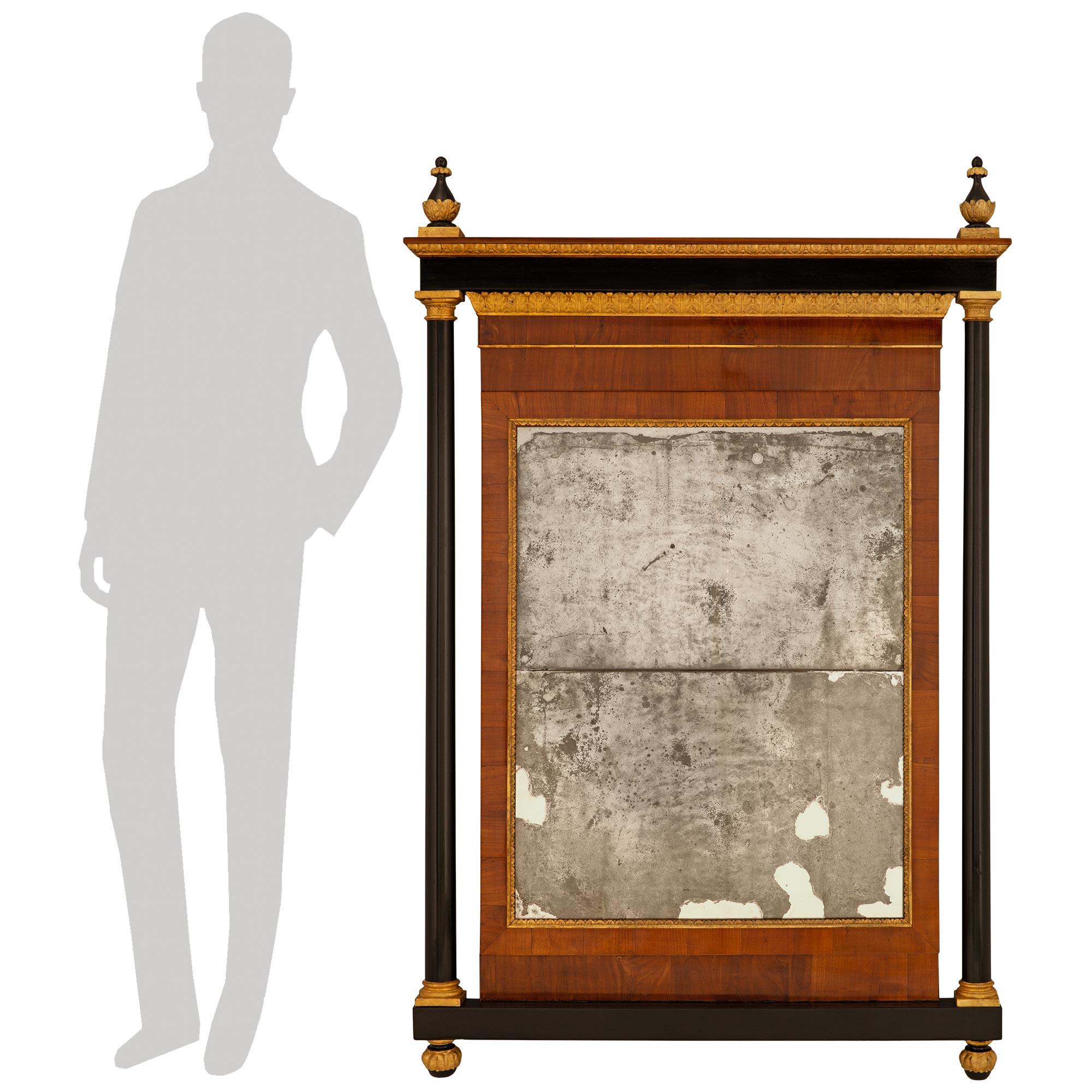 An elegant and most impressive Italian 18th century Louis XVI st. Giltwood, Ebonized Fruitwood, and Walnut mirror, from Lucca. This stunning mirror is raised atop a rectangular ebonized Fruitwood base with two acorn finials accented by Giltwood