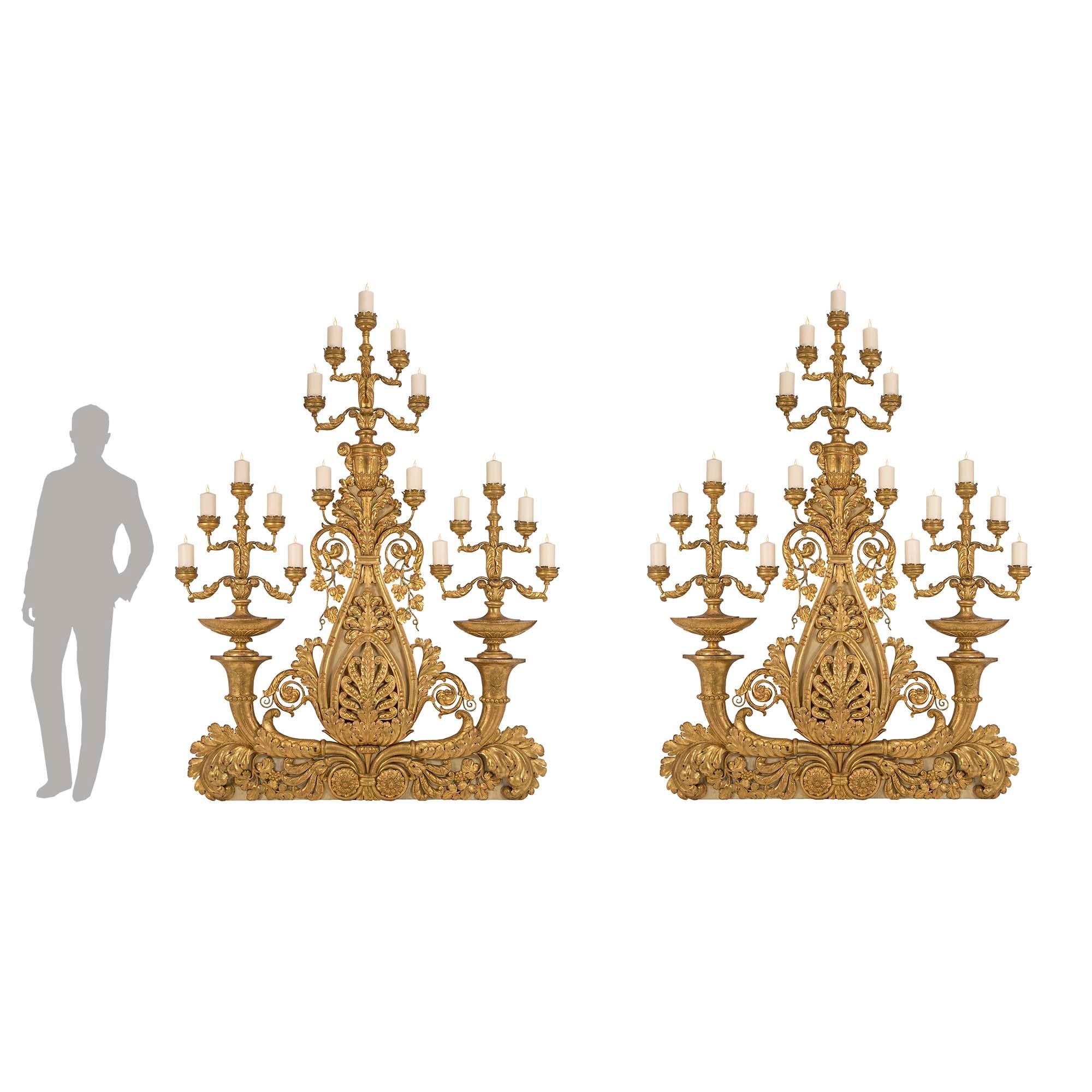A stunning and extremely unique pair of Italian Mid 18th century monumental giltwood and gilt metal candelabras, from Tuscany. Each large scale candelabra is raised on a patinated plinth decorated with opulent and finely carved giltwood scrolled