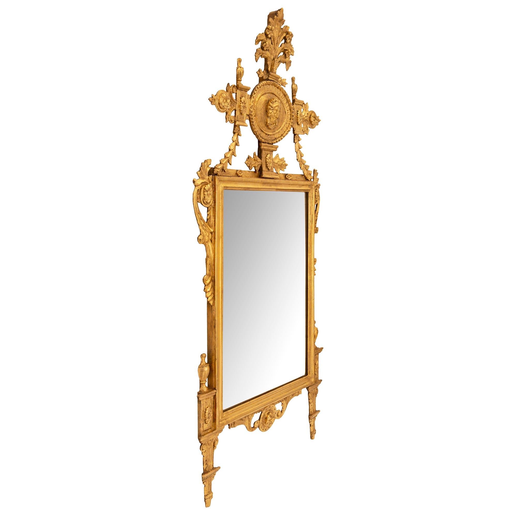 An exceptional and very unique Italian 18th century neo-classical st. giltwood mirror. The mirror retains its original mirror plate set within an elegant wrap around mottled band. The base is centered by a charming richly carved circular floral