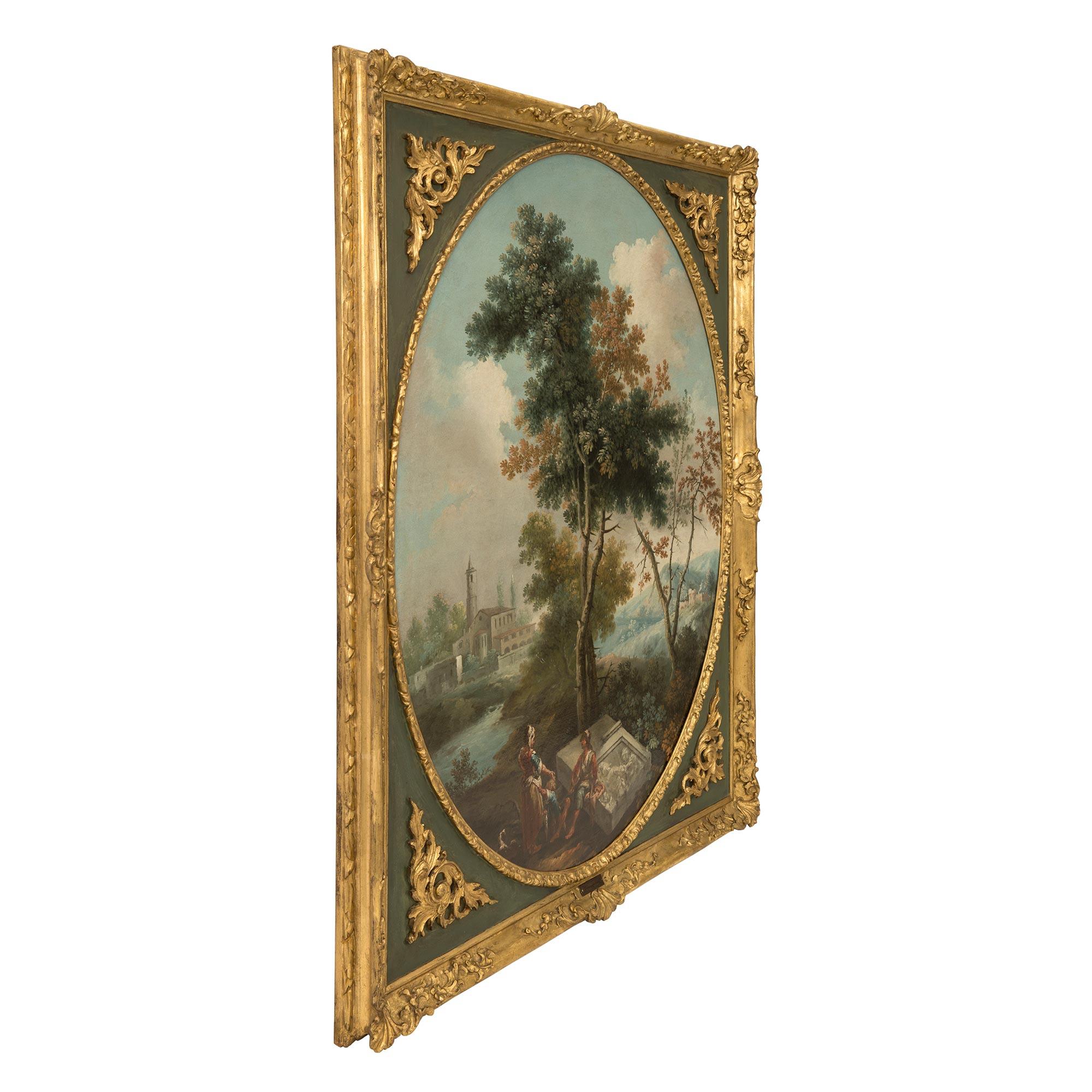 A stunning Italian 18th century Neo-Classical period oil on canvas of a classical landscape scene set in its original giltwood and patinated frame. The charming oval oil on canvas depicts a lovely landscape with a village in the background and a