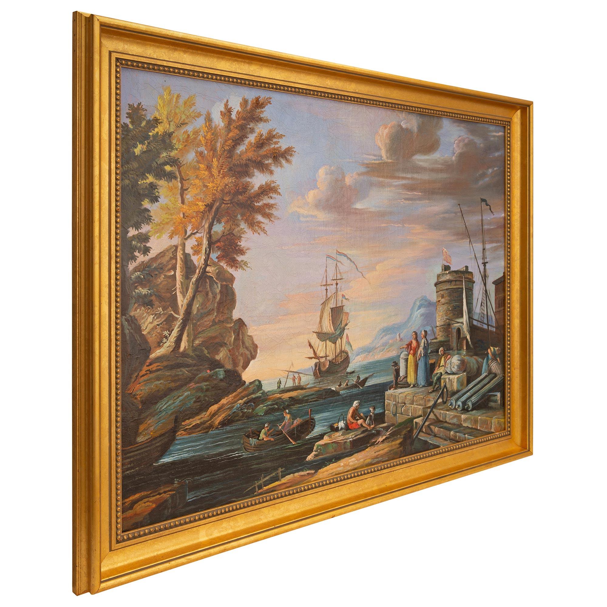 A stunning Italian 18th century oil on canvas painting in a giltwood frame. The painting depicts a calm bay at dusk with an anchored sailboat at the center and the beautiful Italian mountains in the background. At the forefront are charming rowboats