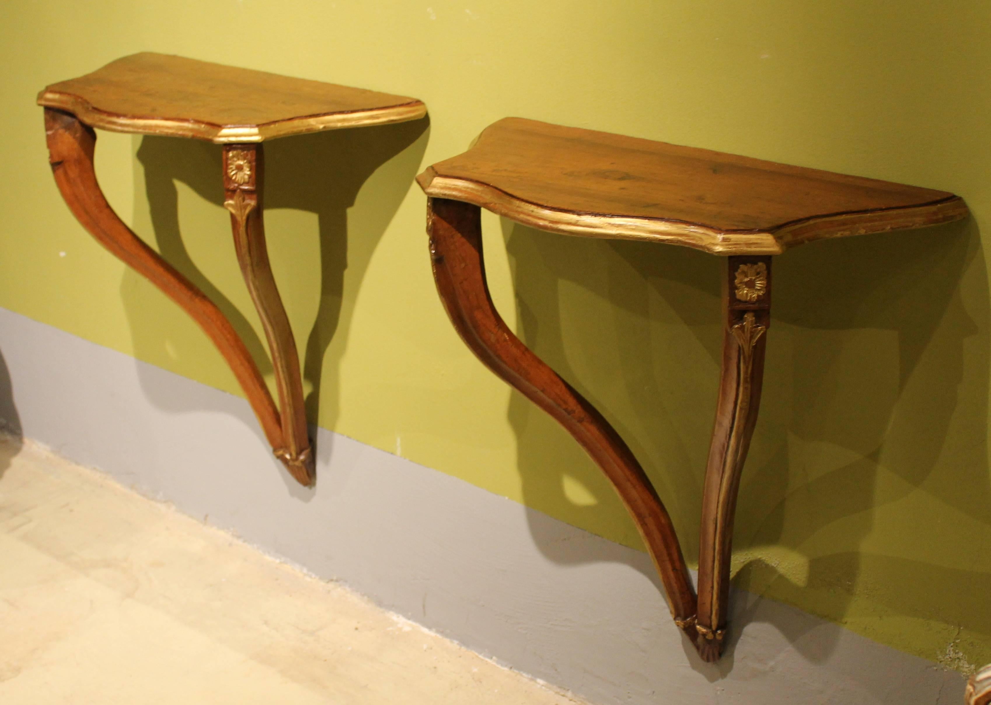 A beautiful pair of serpentine shaped 18th century Venetian wall-mounted consoles in a fantastic rich brown walnut wood with gilt accents ending with two side cabriole legs joined at the bottom. The beautifully curvy shaped top is enriched by a