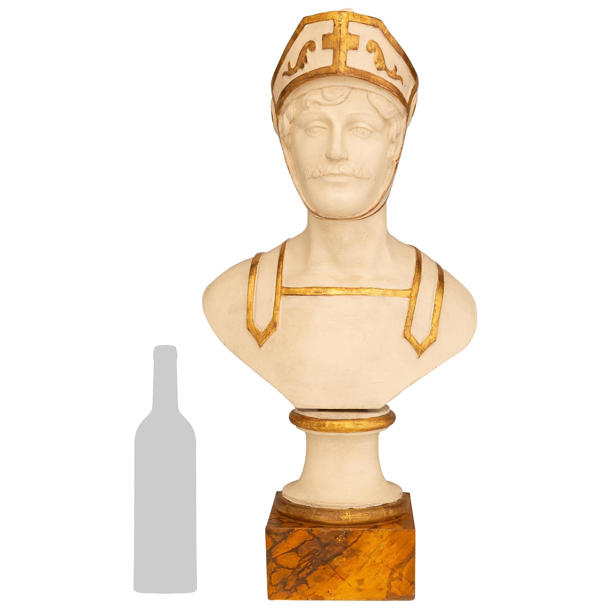 An impressive and most decorative Italian 18th century patinated Wood, Giltwood, and Faux Painted marble bust. This handsome bust of a soldier is raised by its original square faux marble base below a patinated off white circular socle with Giltwood