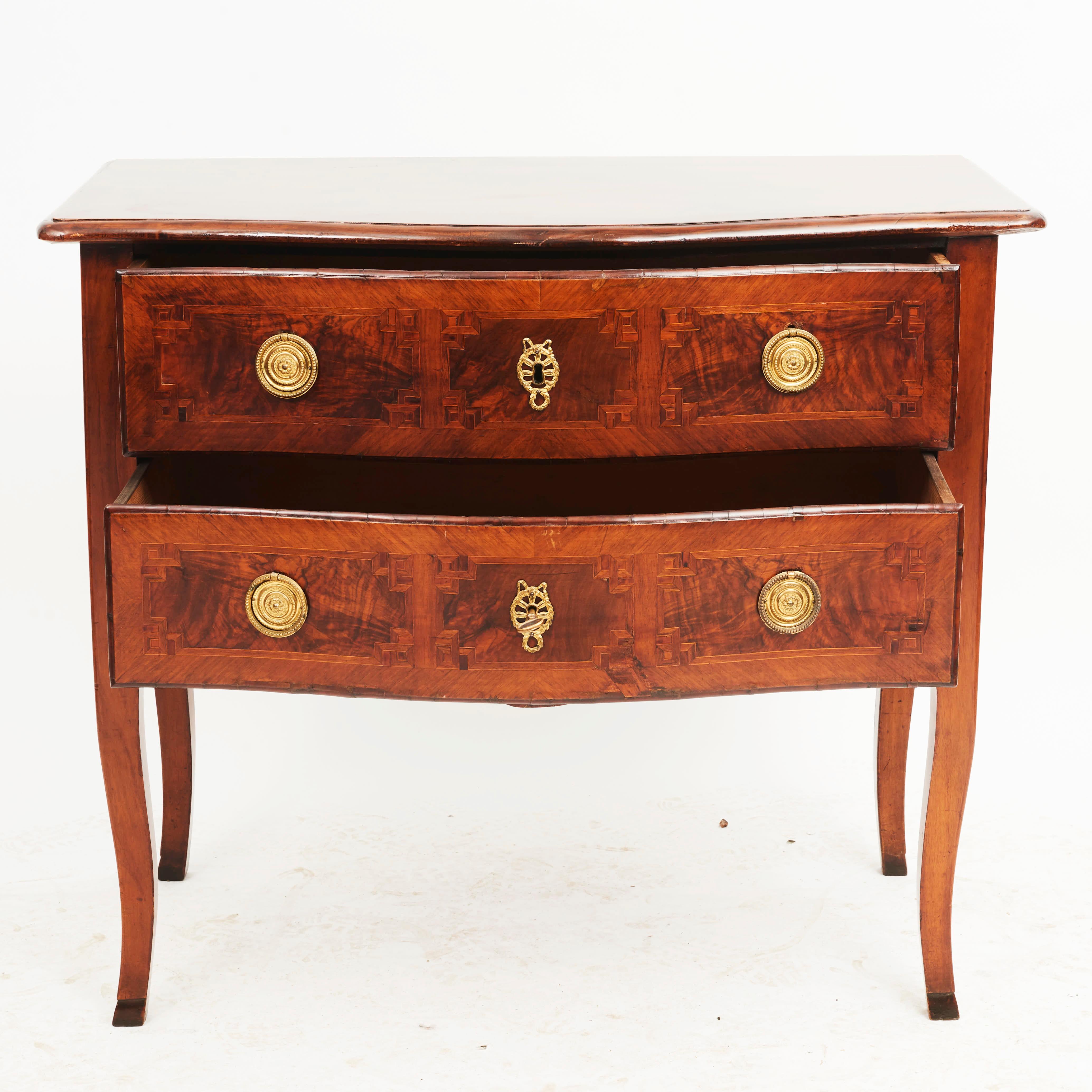 Italian régence two-drawer marquetry commode.
Top in solid walnut, bottom section veneered in walnut. Fronts inlaid with geometric motif borders.
Standing on saber legs ending in feet.
Original condition with a light french polish.
Italy circa