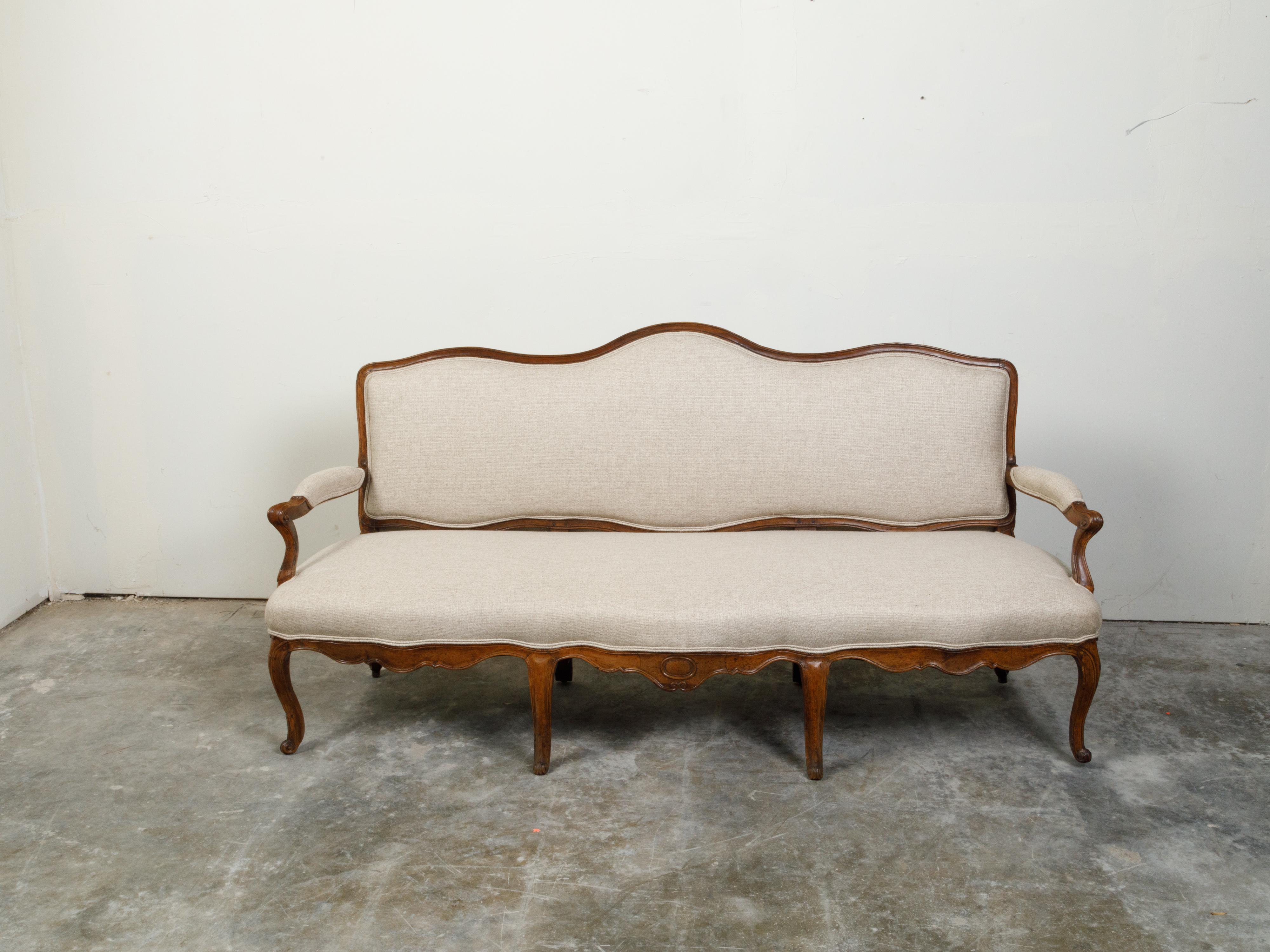 An Italian Rococo walnut sofa from the 18th century, with cabriole legs and new upholstery. Created in Italy during the 18th century, this walnut sofa features a rectangular back with serpentine lines, connected to two open arms with scrolling