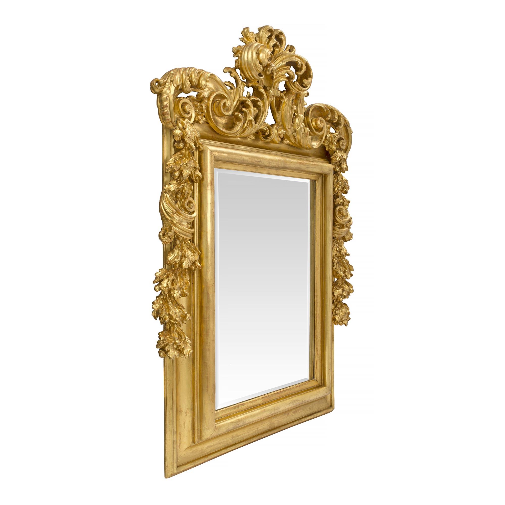 A magnificent and high quality Italian 18th century Roman rectangular giltwood mirror. The beveled mirror is within a handsome wide moulded giltwood frame. At the very impressive top crown is a robust pierced scrolled design of large opulent