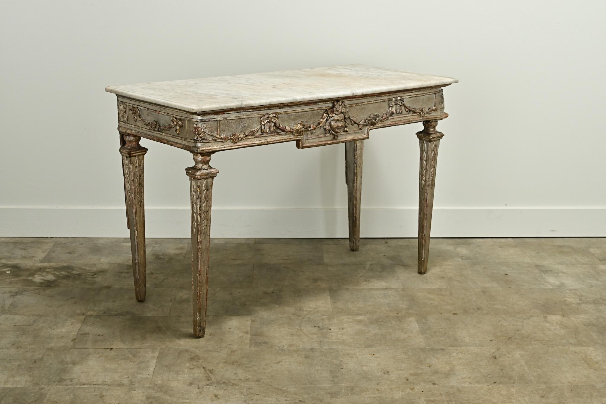 An impressive silver-gilt Italian console from the late 18th Century. The worn and patinated white marble top is smooth and makes for a durable surface. The base is hand carved with floral swags, bows and a cameo in the center. The legs are tapered