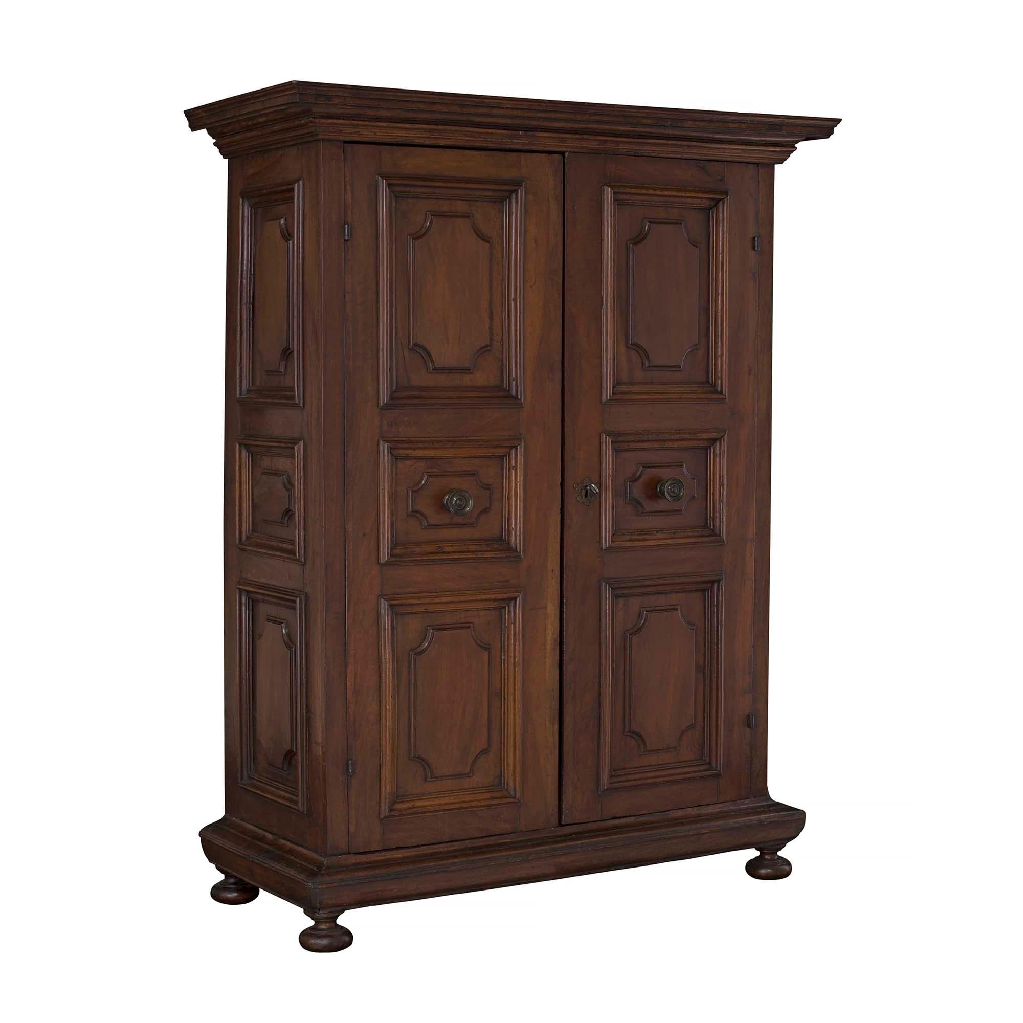 A handsome Italian 18th-century solid walnut and iron Tuscan armoire. The armoire is raised by bun feet below the straight mottled frieze. At the center are two beautiful doors with carved recessed panels and a central circular iron pull. The doors