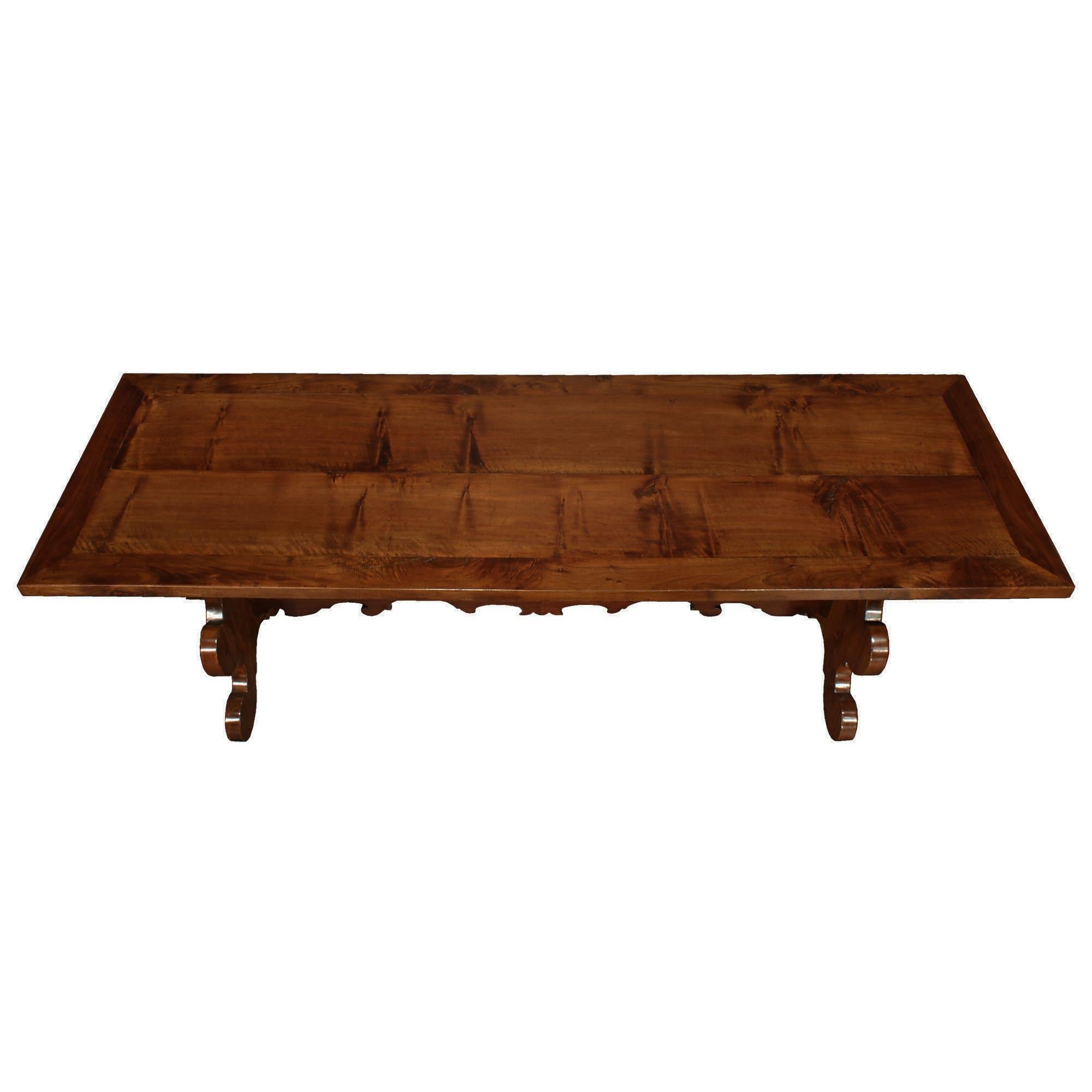 A handsome Italian 18th century solid walnut trestle table from Tuscany. The table is raised by two thick carved scalloped supports joined by an impressive foliate carved stretcher secured by a tapered peg. Above is the large rectangular solid